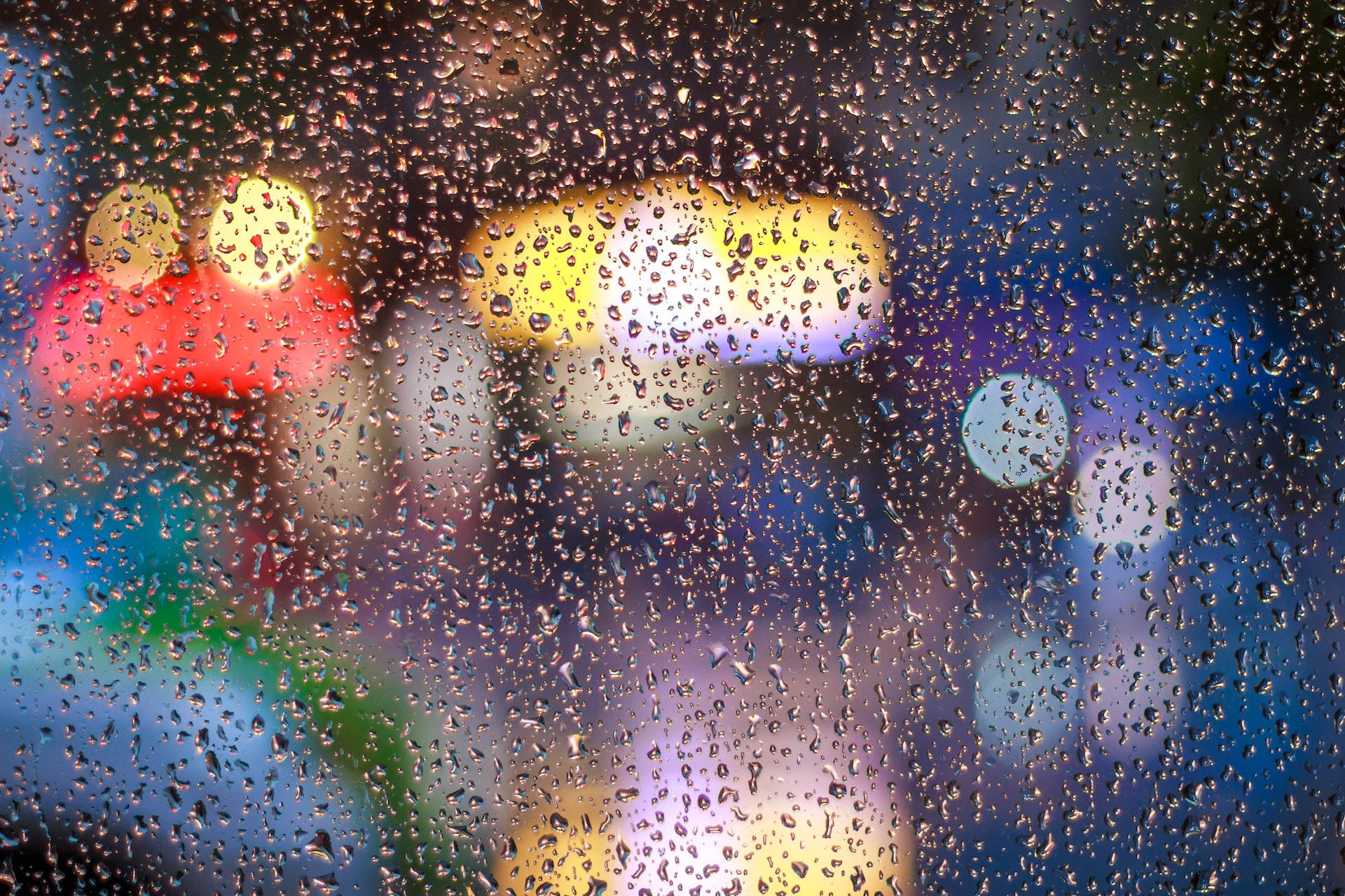 Light 桌布 壁紙 — 雨滴依附在窗戶上，顯露出溫暖的紅色、黃色和冷藍色的模糊城市燈光。