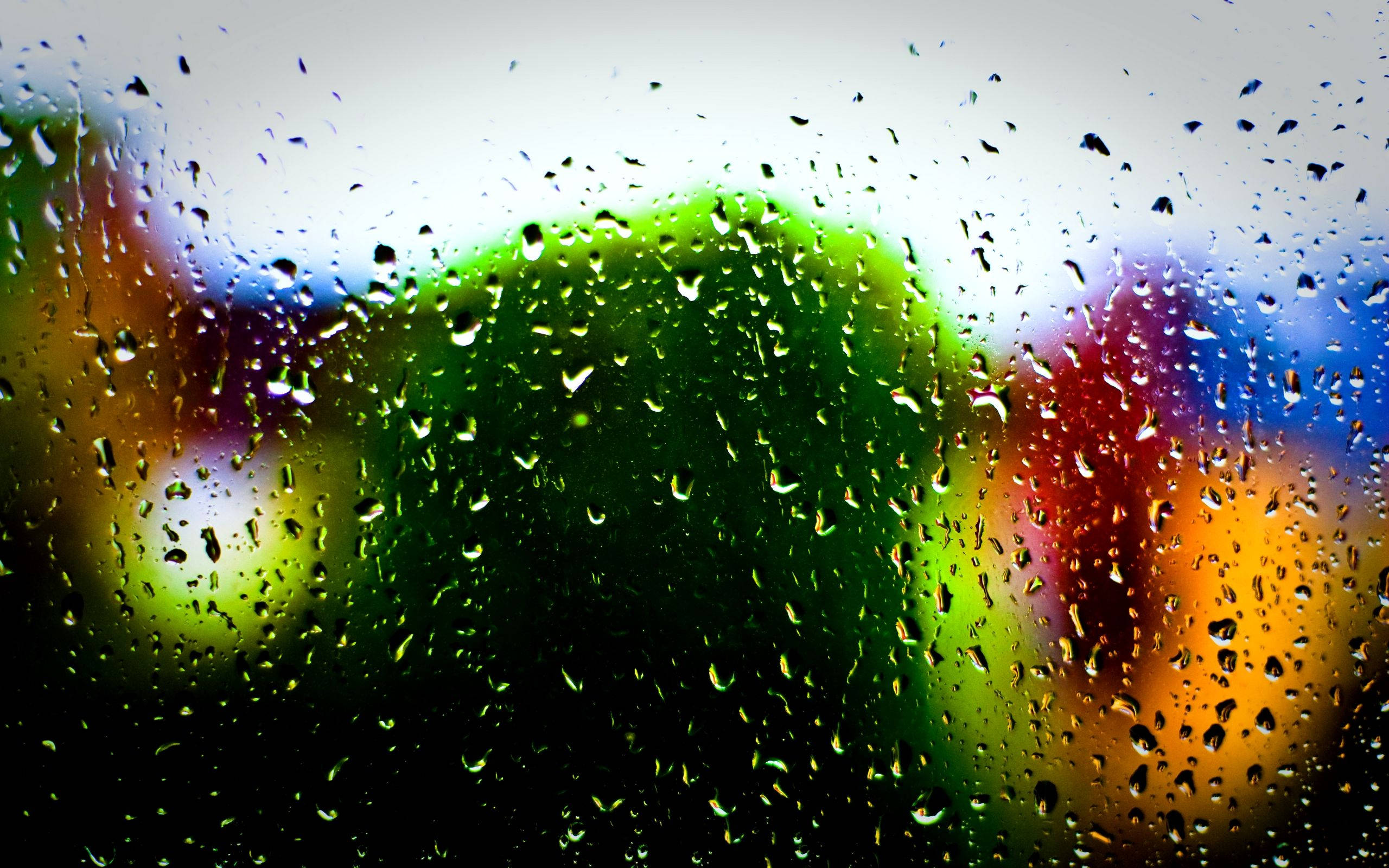 Rainy Day 桌布 壁紙 — 雨滴依附在窗戶上，顯露出窗外街燈和樹葉模糊而鮮豔的色彩。