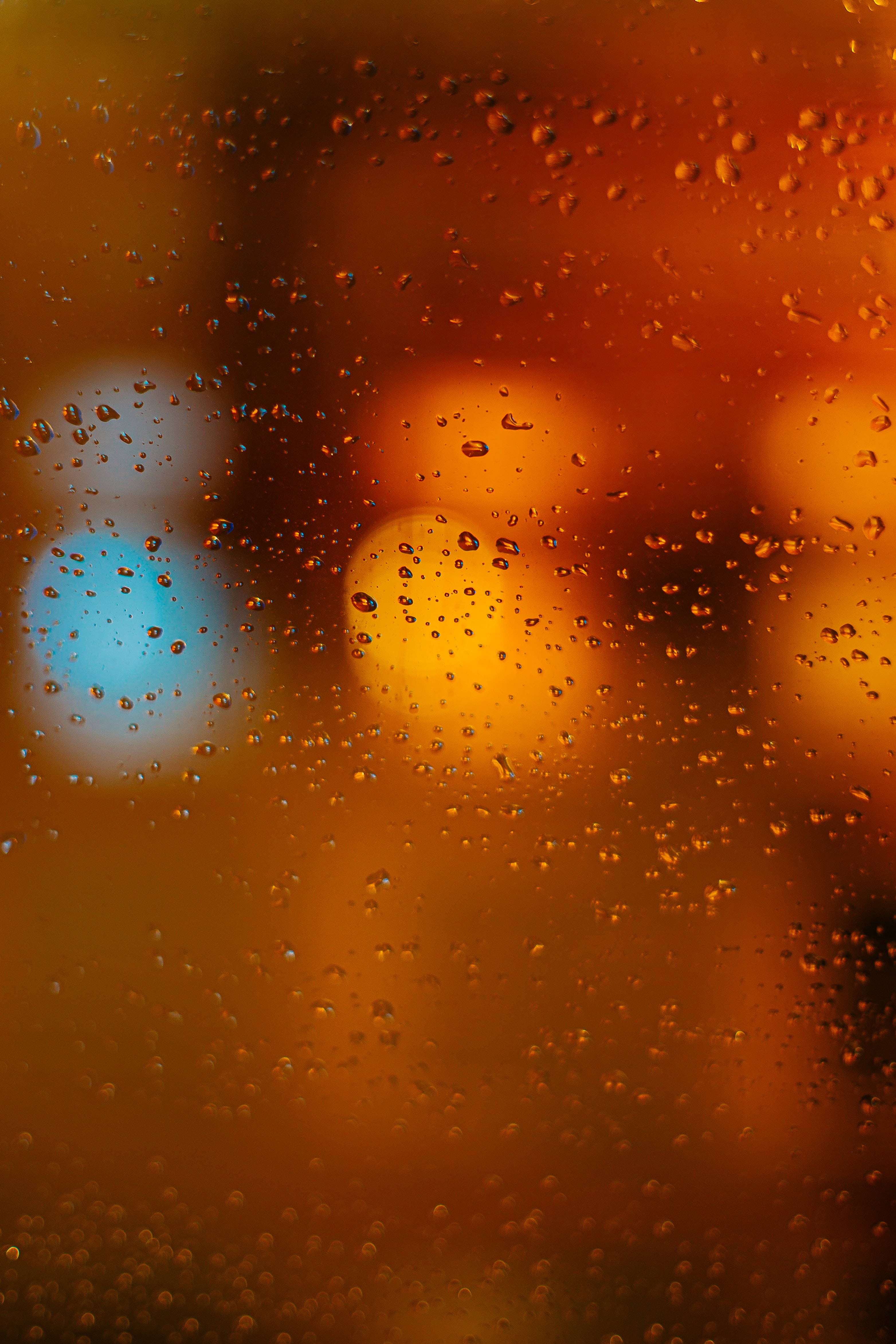 焦點 桌布 壁紙 — 雨滴依附在窗戶上，顯露出遠處模糊的橙色和藍色城市燈光。