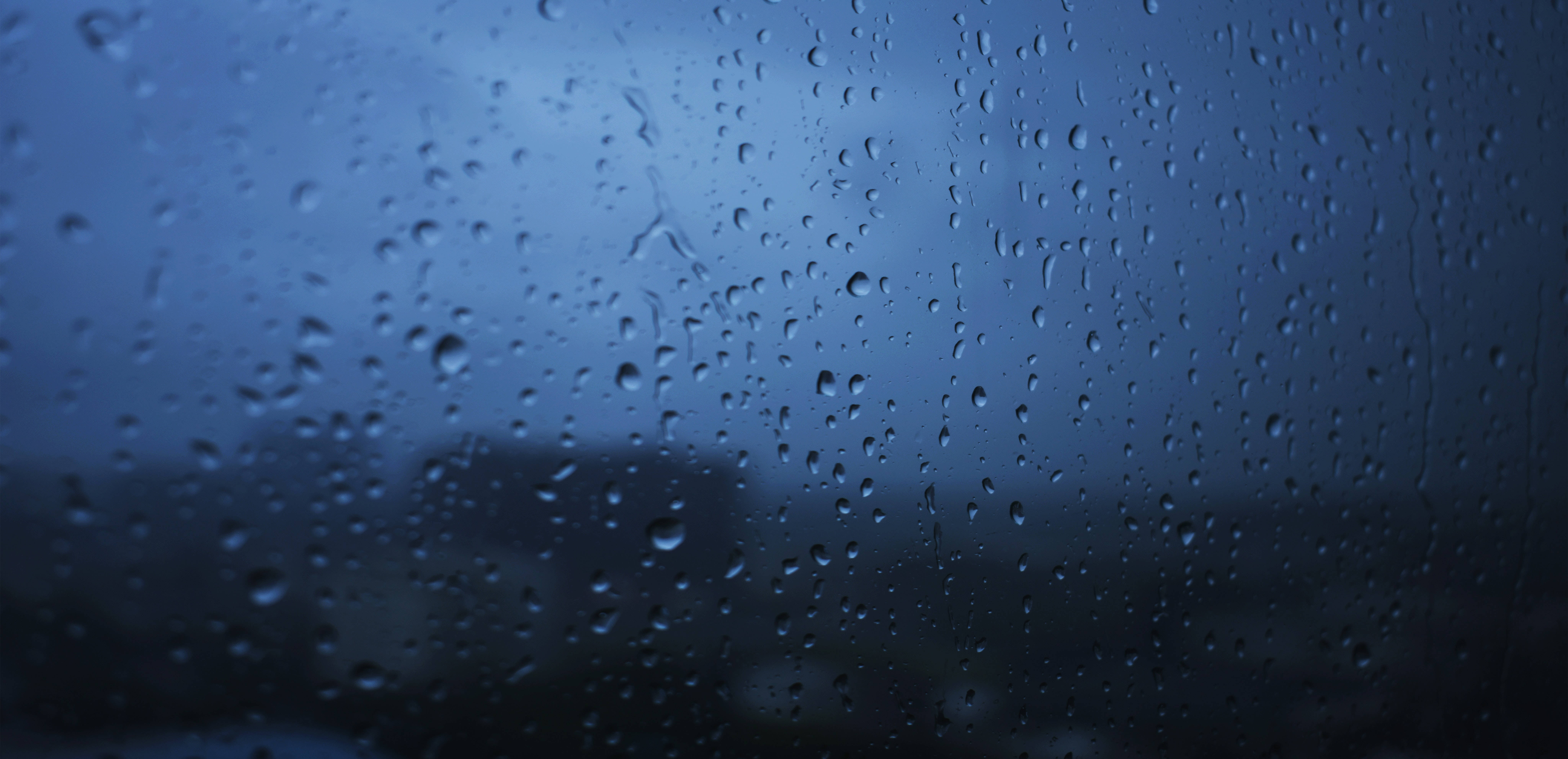 Transparent 桌布 壁紙 — 雨滴依附在窗玻璃上，模糊了暴風雨天空下的深藍色城市天際線。