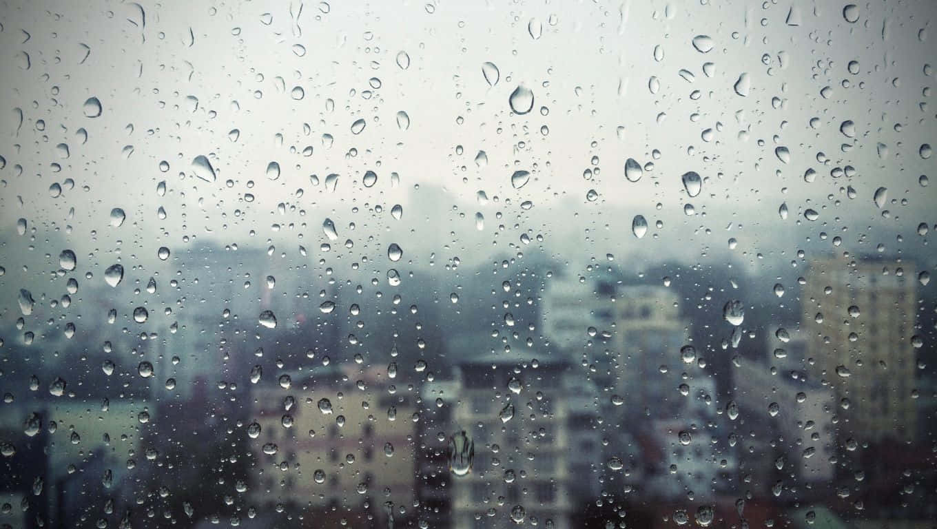 1360x768 桌布 壁紙 — 雨滴依附在窗玻璃上，模糊了陰天下的朦朧城市天際線。