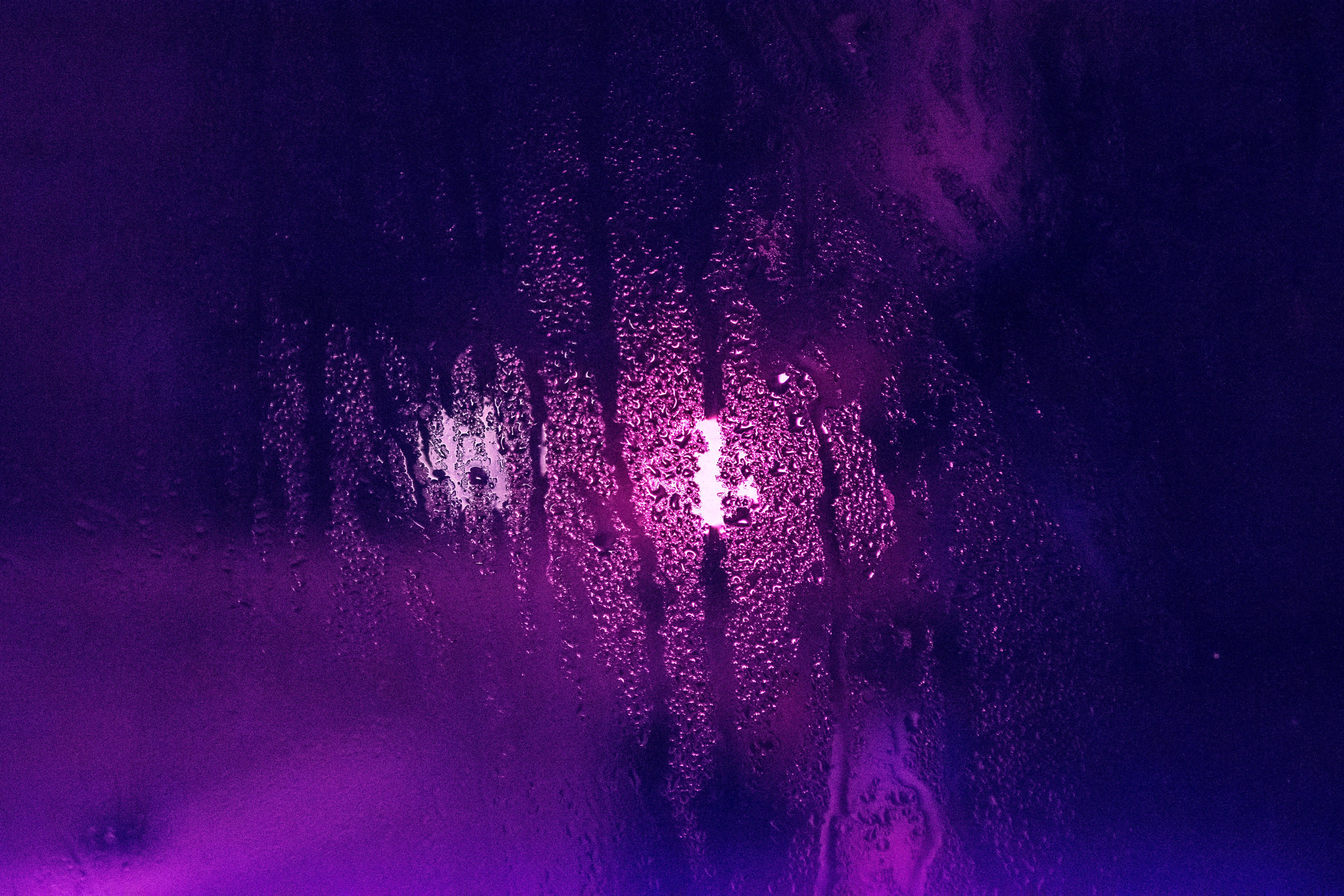 Dark Purple Desktop 桌布 壁紙 — 雨滴劃過一扇窗戶，窗戶在黑暗背景下散發著充滿活力的紫色和粉紅色霓虹燈光。