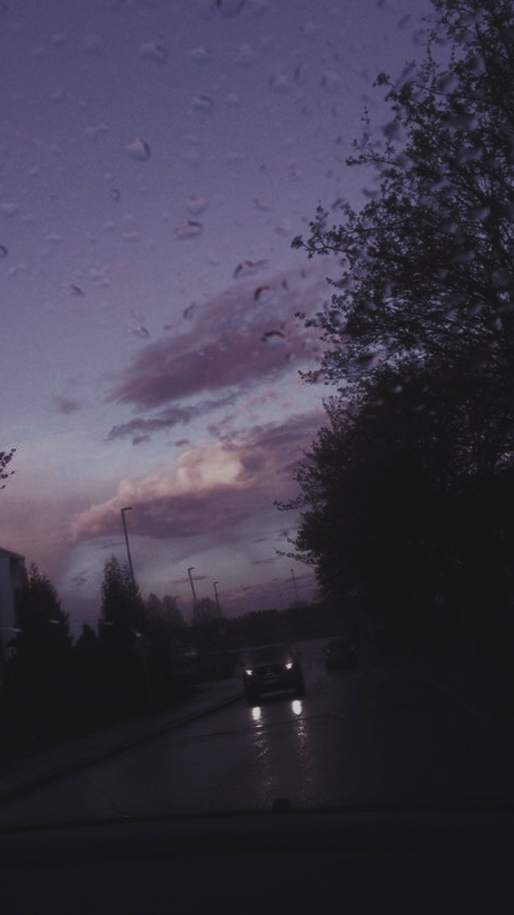 Purple Aesthetic Phone 桌布 壁紙 — 雨滴劃過擋風玻璃，汽車在紫色暮色天空下行駛在濕漉漉的街道上。