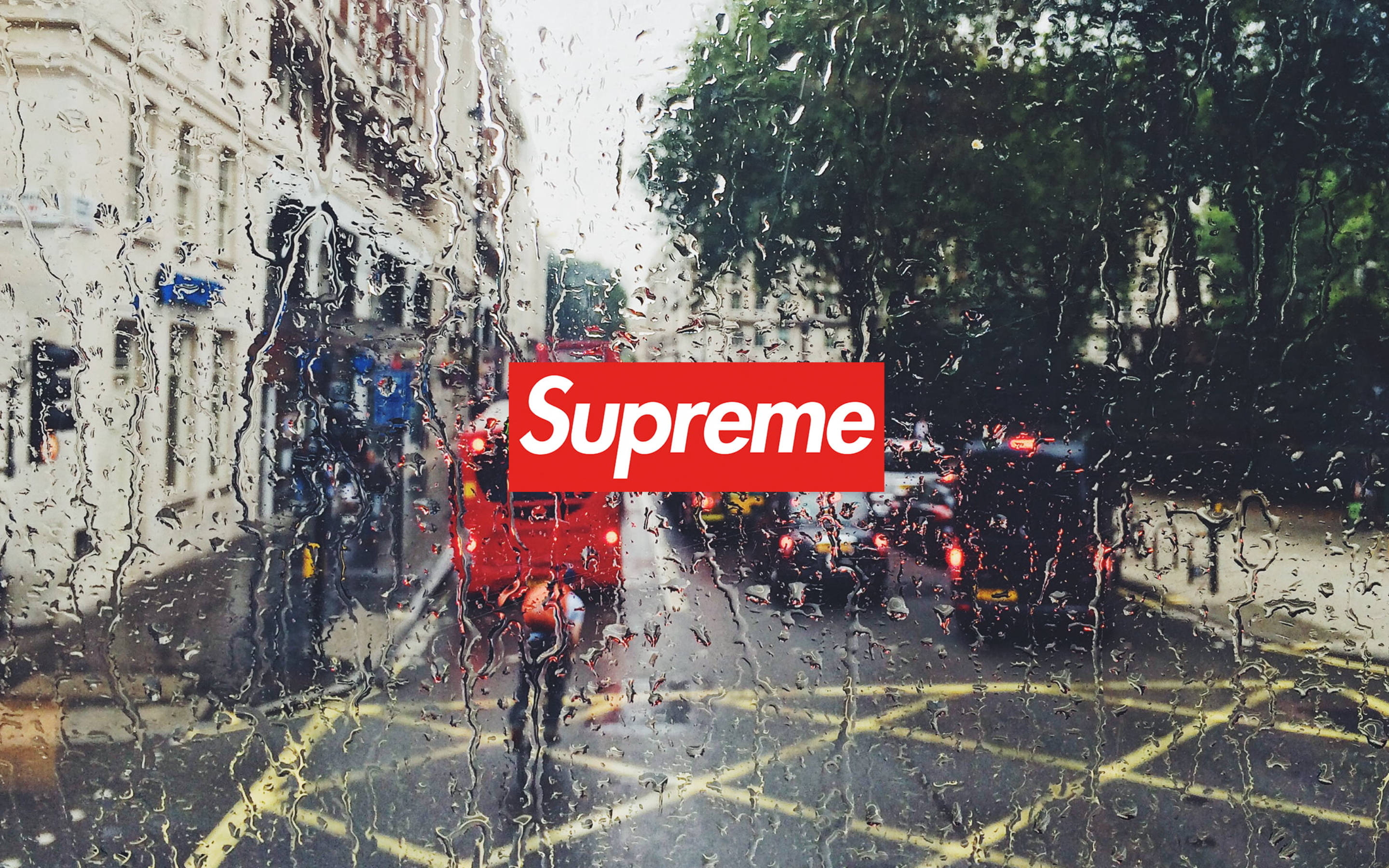 Dope Supreme 桌布 壁紙 — 雨滴劃過汽車車窗，俯瞰濕漉漉的城市街道，有一輛紅色雙層巴士和顯眼的紅色Supreme標誌。