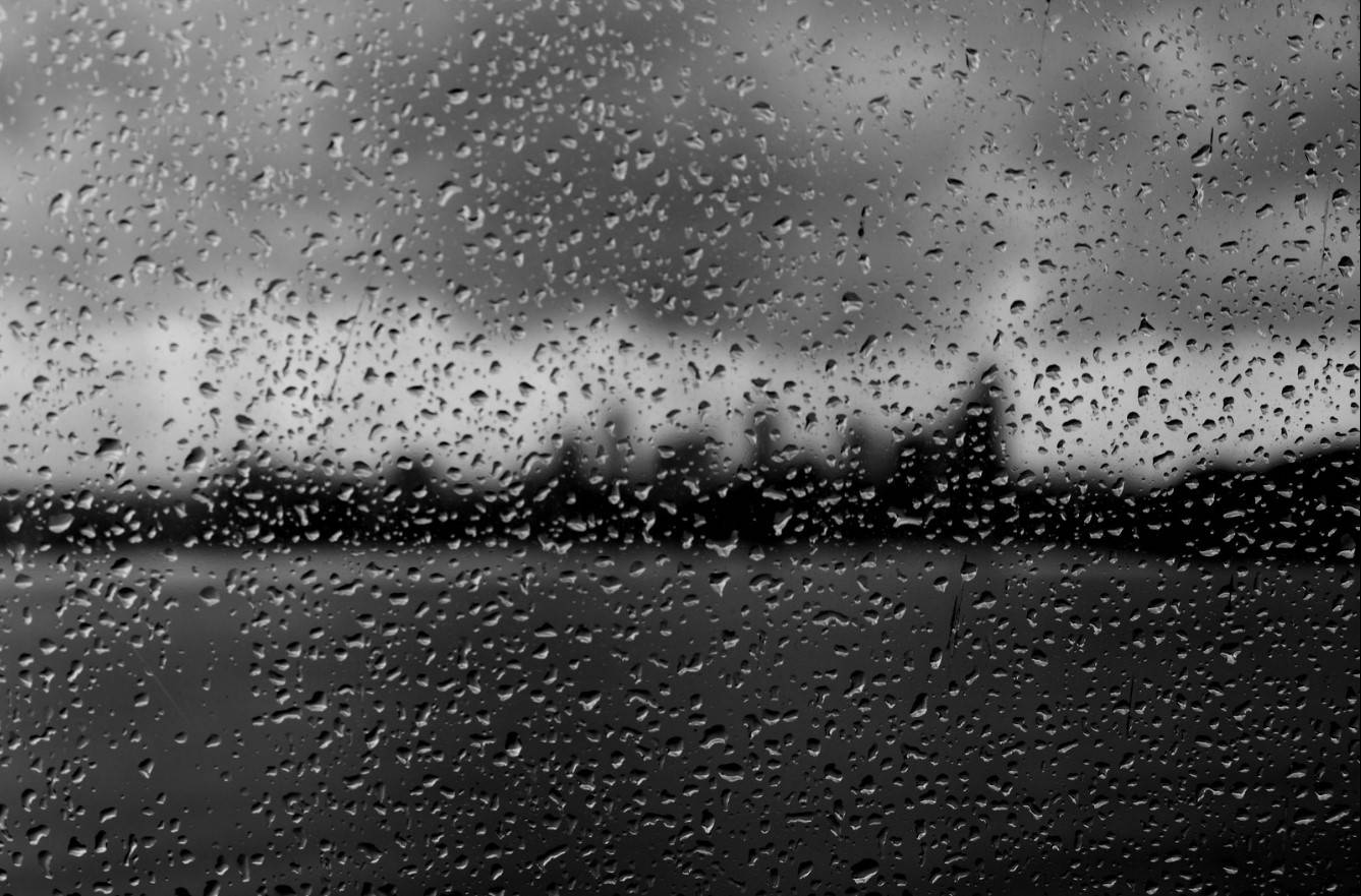 Raindrops 桌布 壁紙 — 雨滴劃過玻璃窗，模糊了陰天下單色的城市景觀。
