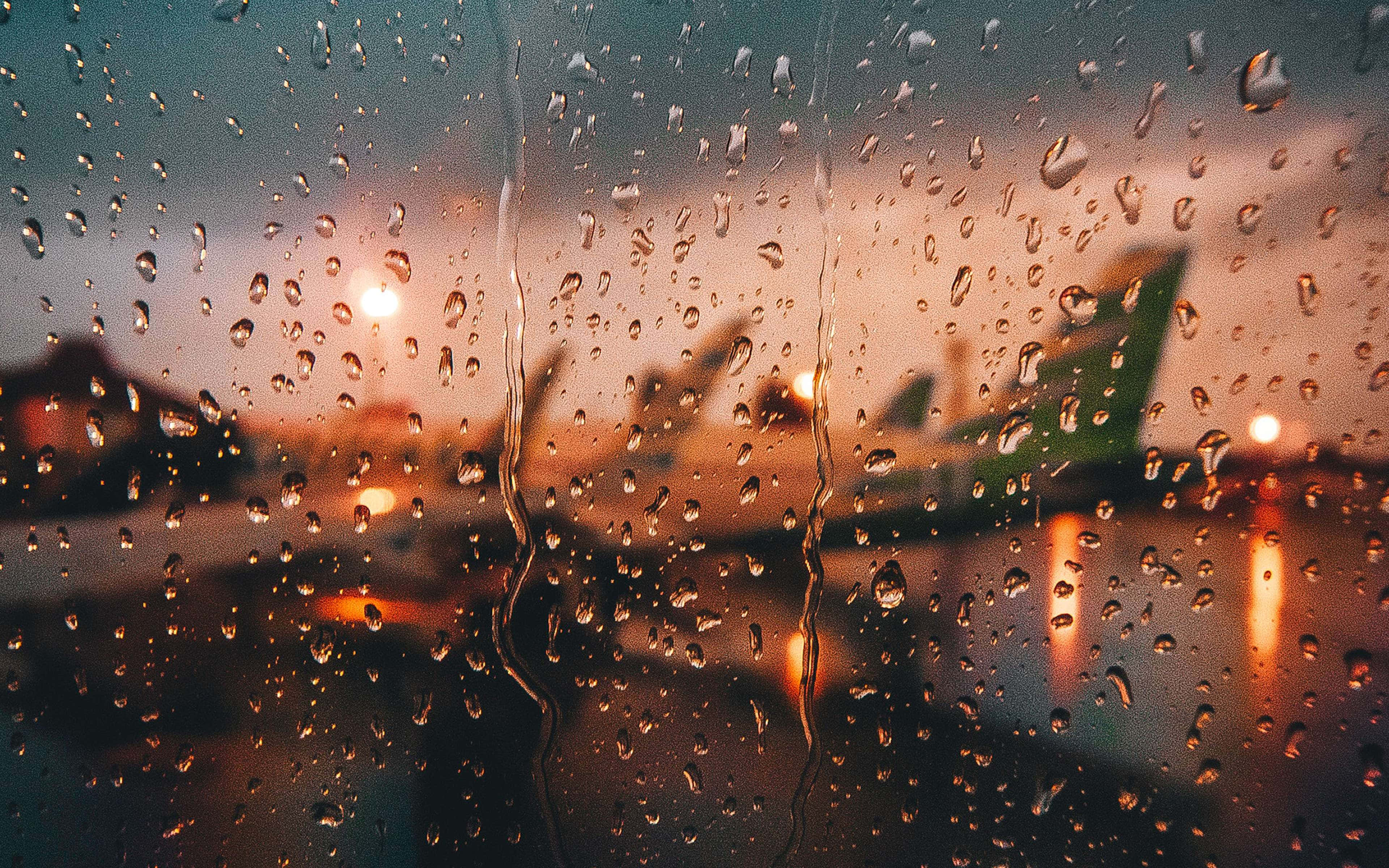 Rain 4K 桌布 壁紙 — 雨滴劃過窗戶，在溫暖的暮光下顯現出模糊的機場飛機。