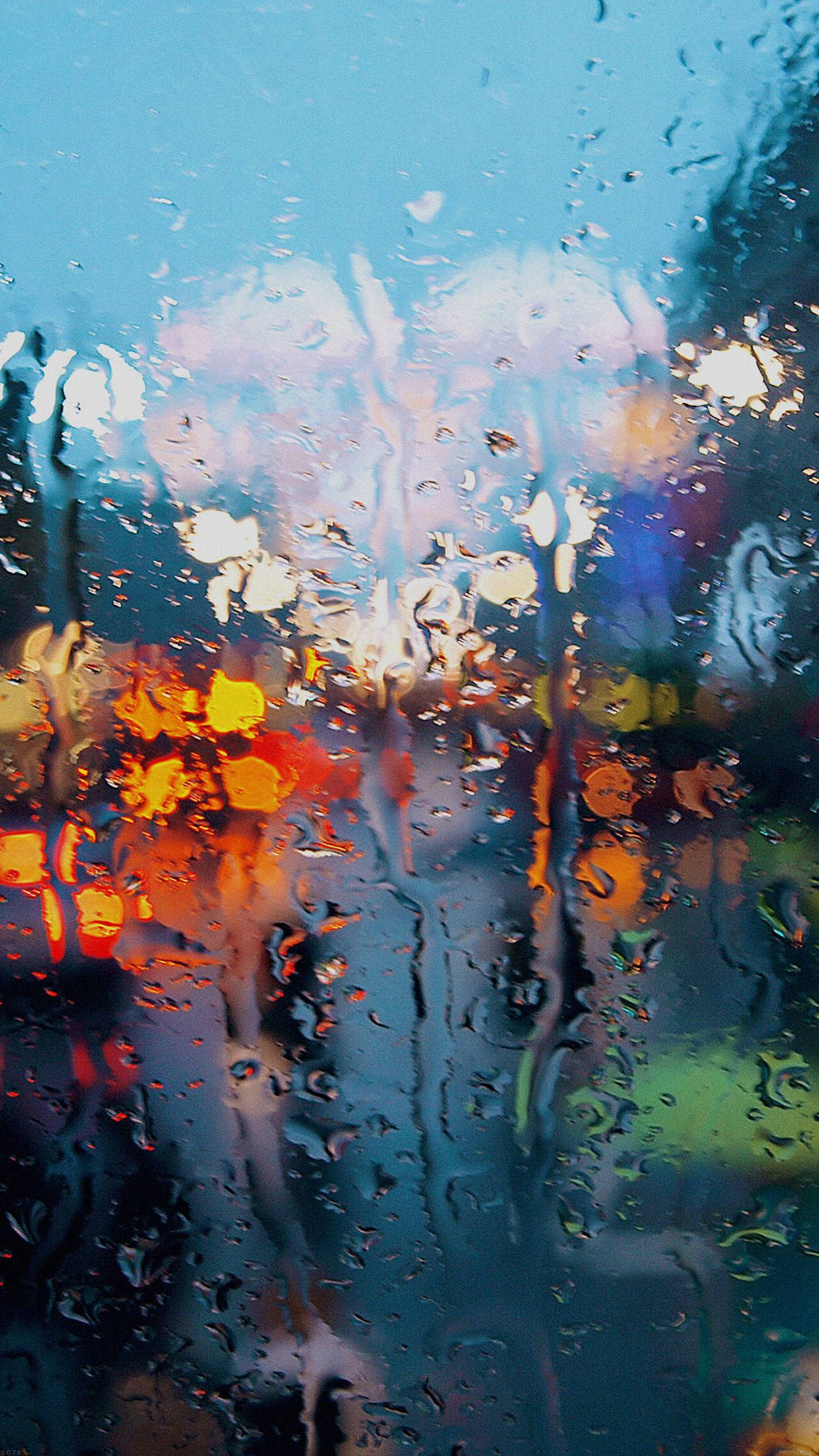 iPhone 桌布 壁紙 — 雨滴劃過窗戶，將充滿活力的城市燈光模糊成柔和的發光條紋，映襯著涼爽的藍色暮色天空。