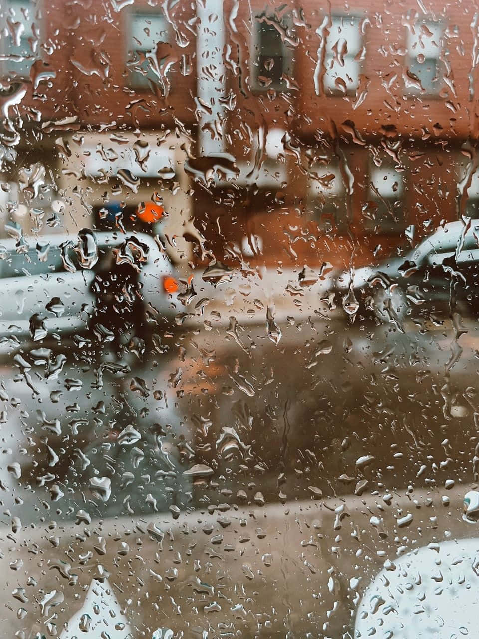 Aesthetic Rain 桌布 壁紙 — 雨滴劃過窗戶，顯露出模糊的城市街道，有一個人撐著橙色雨傘。