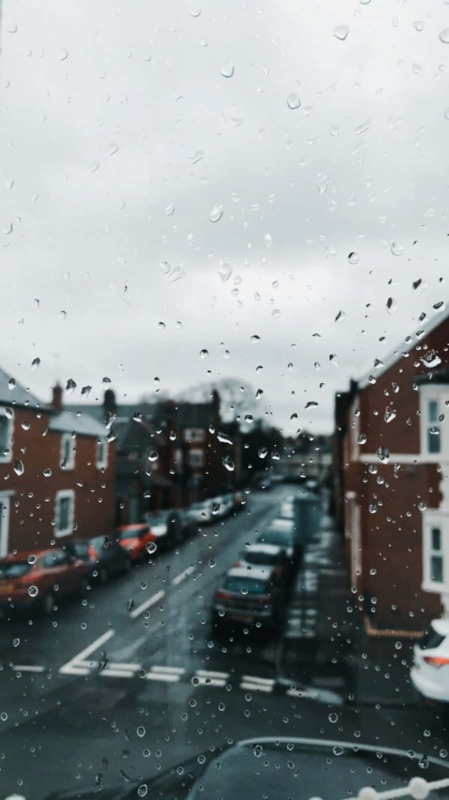 Aesthetic Rain 桌布 壁紙 — 雨滴劃過車窗，俯瞰濕漉漉的城市街道，兩旁是紅磚建築，天空陰沉。