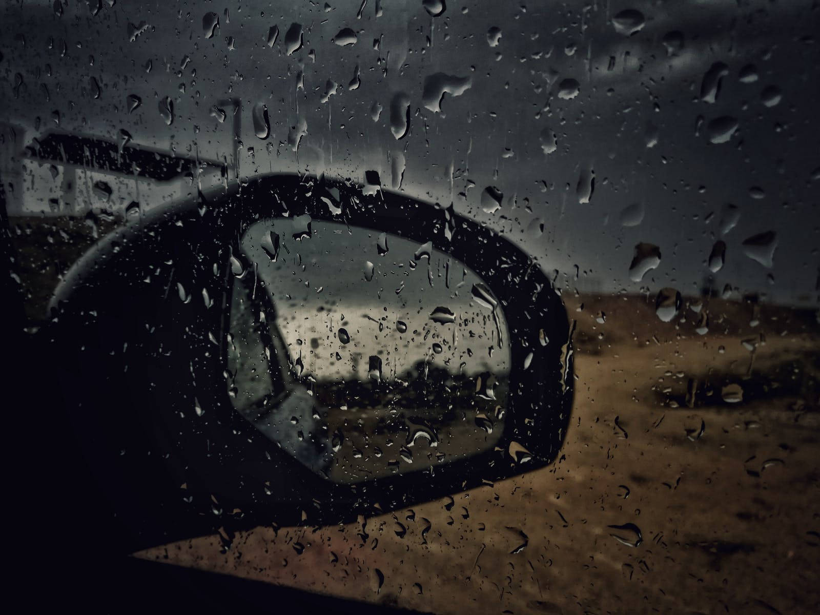 Raining 桌布 壁紙 — 雨滴劃過車窗，透過側鏡反射出陰沉的路邊景象。