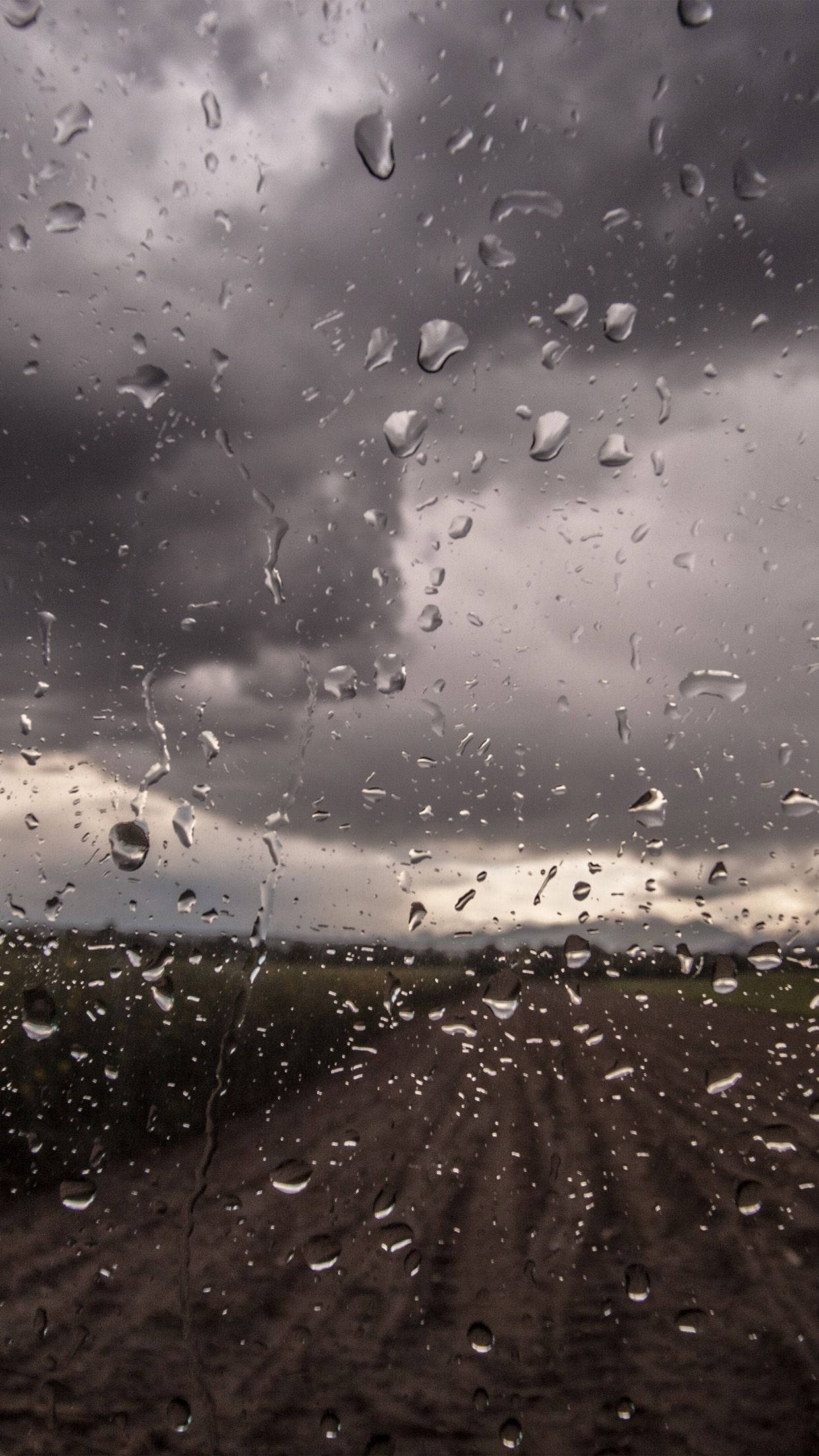 桌布 壁紙 — 雨滴劃過車窗，露出陰沉多雲的天空和遠處泥濘的田野。