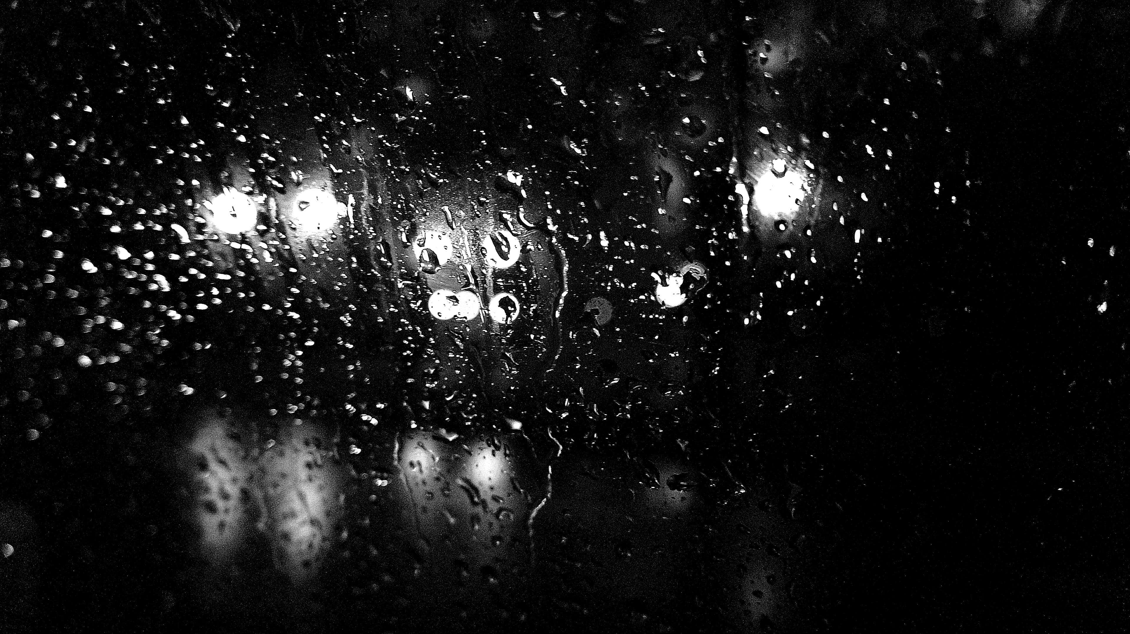 桌布 壁紙 — 雨滴劃過黑暗的窗戶，反射出模糊的城市燈光，呈現單色調。
