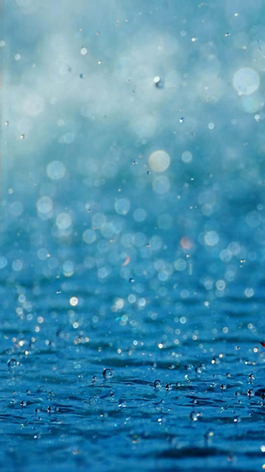 下雨 桌布 壁紙 — 雨滴在充滿活力的藍色水面上飛濺閃爍，營造出閃閃發光的散景效果。