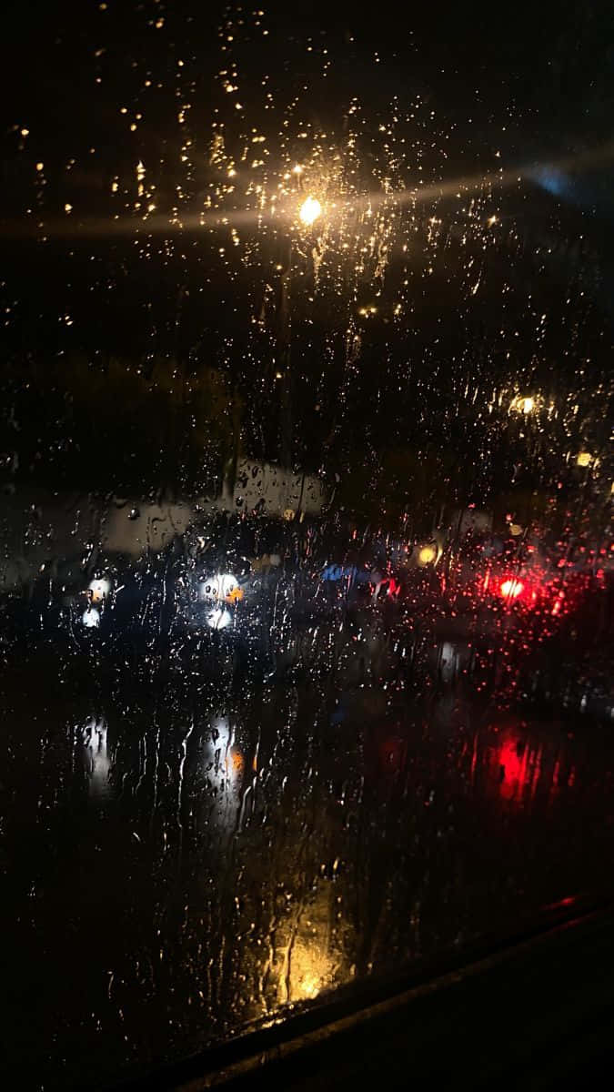 window 桌布 壁紙 — 雨滴在夜間劃過車窗，反射出閃爍的路燈和模糊的車尾燈。
