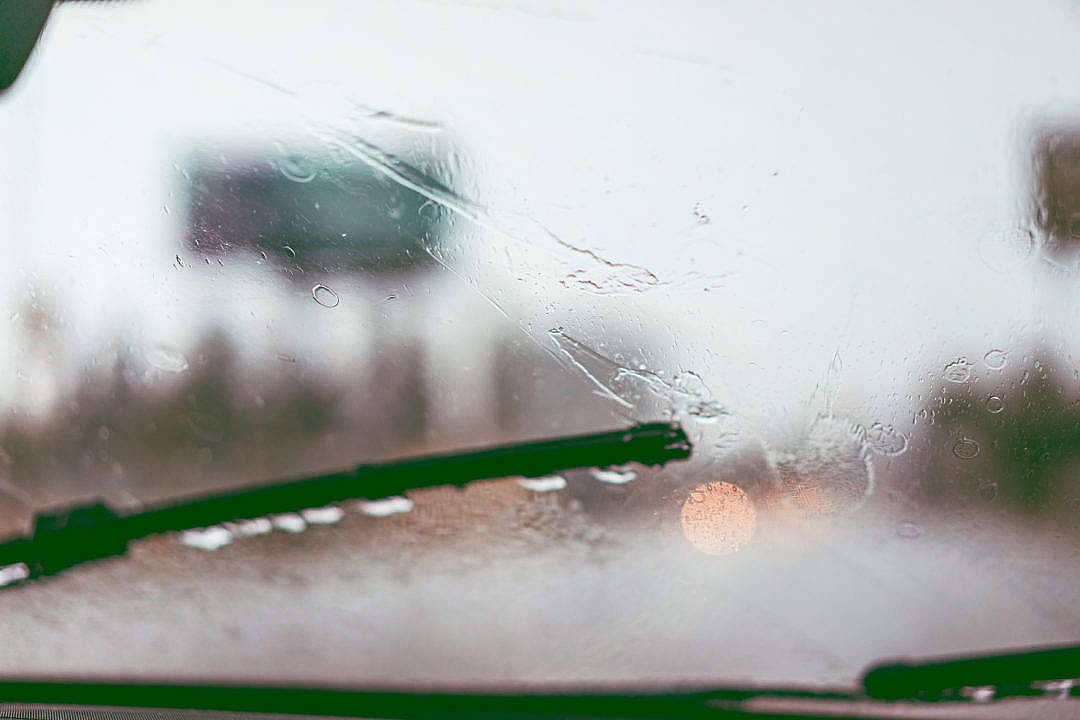 Raining 桌布 壁紙 — 雨滴在汽車擋風玻璃上劃過，綠色雨刷在移動，背景是模糊的雨街景。
