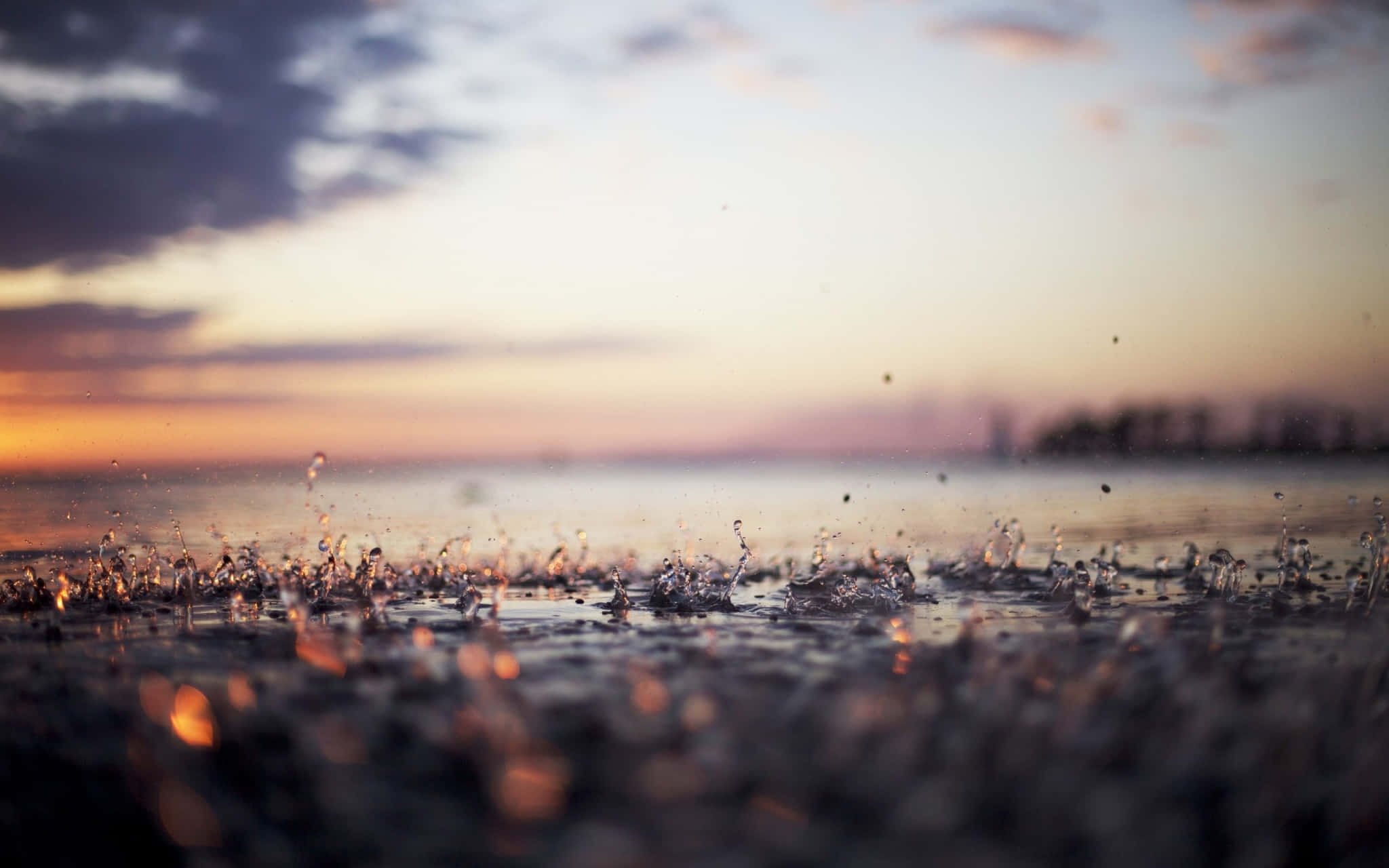 下雨 桌布 壁紙 — 雨滴在潮濕的地面上生動地濺起，柔和的夕陽將天空染成溫暖的橙色和紫色。