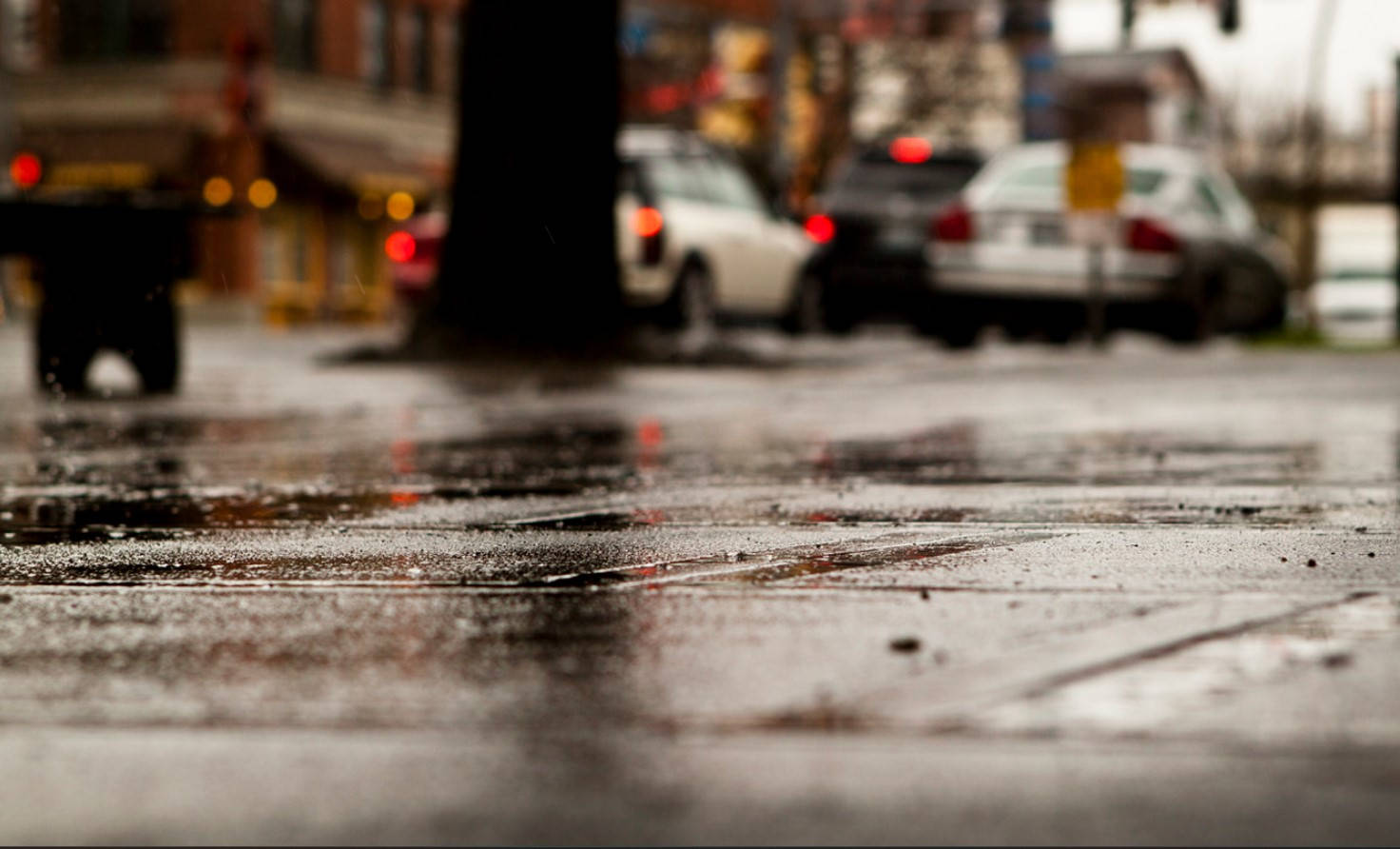 Rainy Day 桌布 壁紙 — 雨滴在濕漉漉的城市人行道上閃閃發光，模糊的汽車和街燈在背景中發光。
