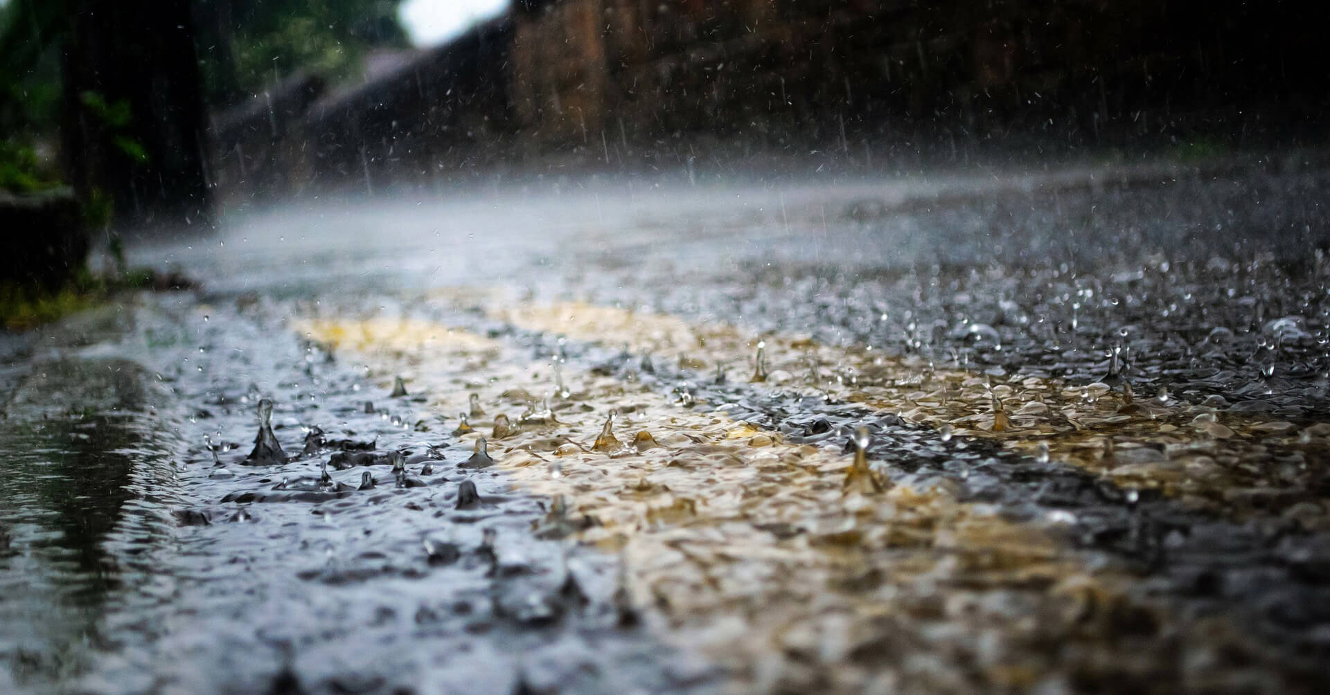 Raining 桌布 壁紙 — 雨滴在濕漉漉的瀝青路上飛濺並泛起漣漪，反射出模糊背景中柔和的金色光芒。