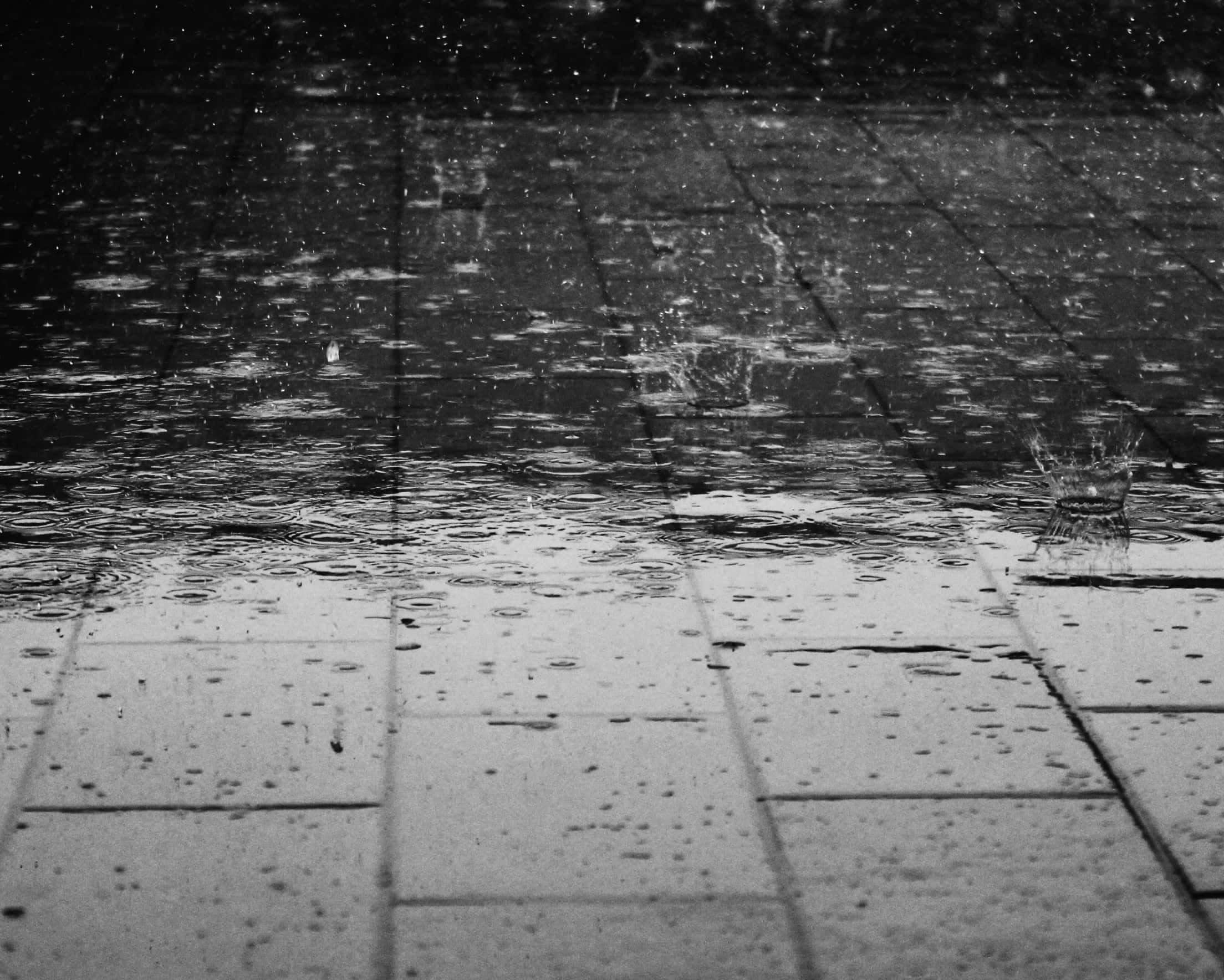 2208x1768 桌布 壁紙 — 雨滴在濕透的磁磚路面上濺起漣漪，黑白畫面捕捉了傾盆大雨的寧靜節奏。