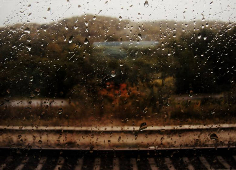 Raining 桌布 壁紙 — 雨滴在火車窗上劃過，模糊的秋樹和軌道在憂鬱的黑白場景中掠過。