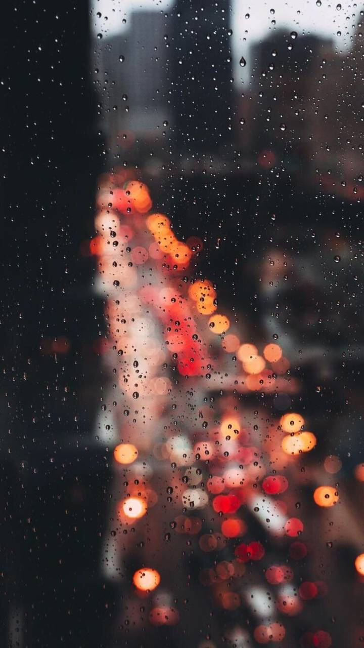 Dslr 桌布 壁紙 — 雨滴在窗戶上劃出條紋，顯露出模糊的城市燈光，在黑暗的城市背景下溫暖地發光。