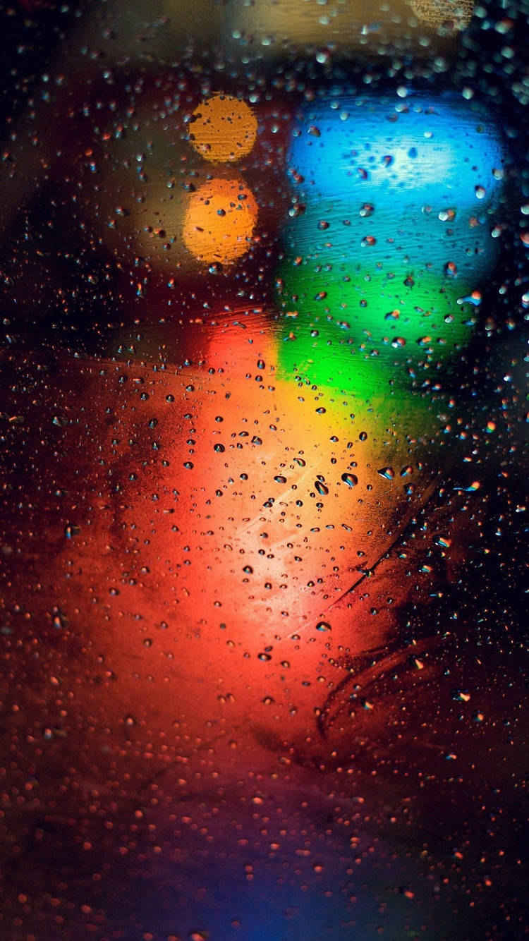 iPhone 桌布 壁紙 — 雨滴將夜間濕窗上充滿活力的城市燈光模糊成發光的散景。