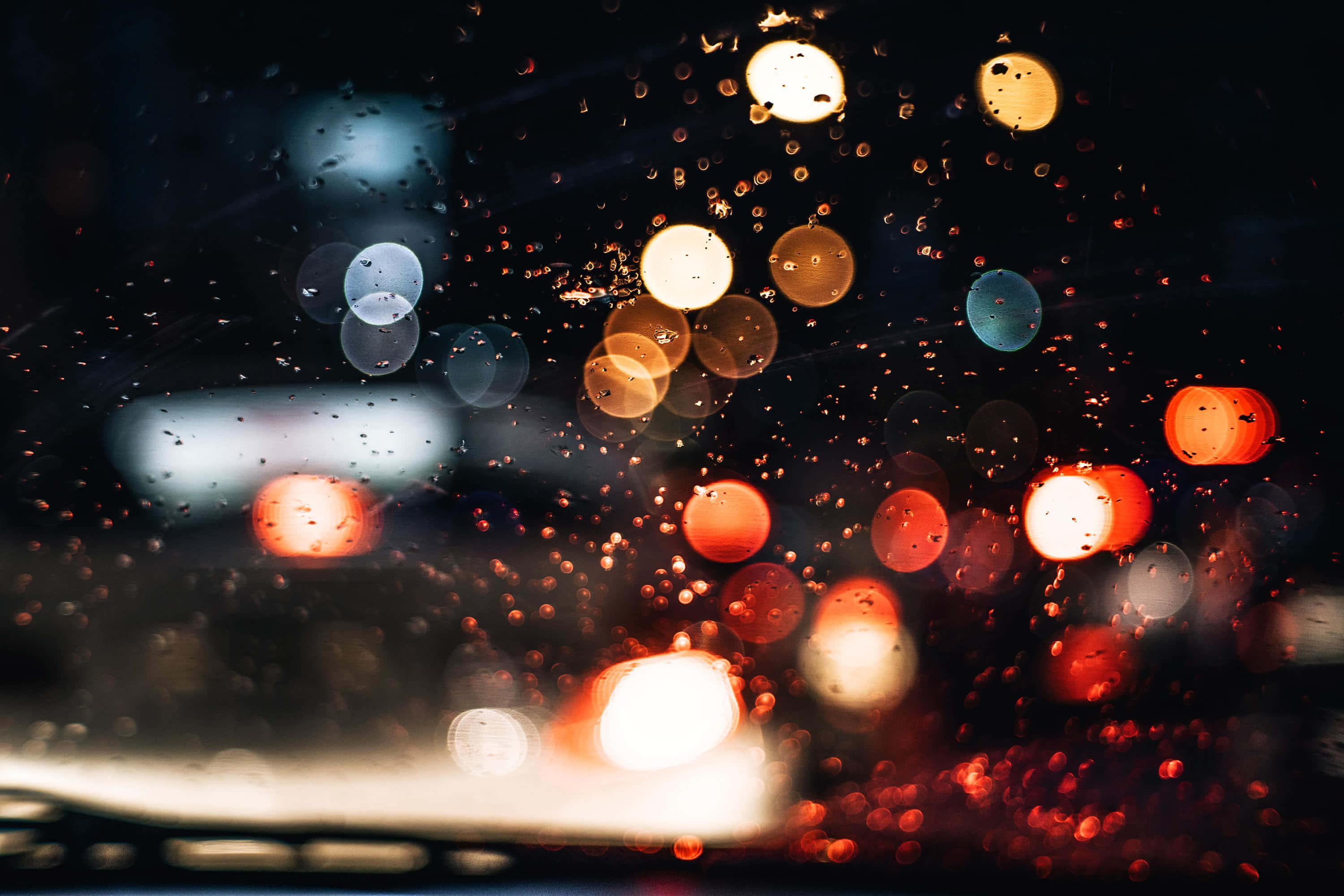 Bokeh 桌布 壁紙 — 雨滴將汽車擋風玻璃上充滿活力的城市燈光模糊成發光球體，在夜晚。
