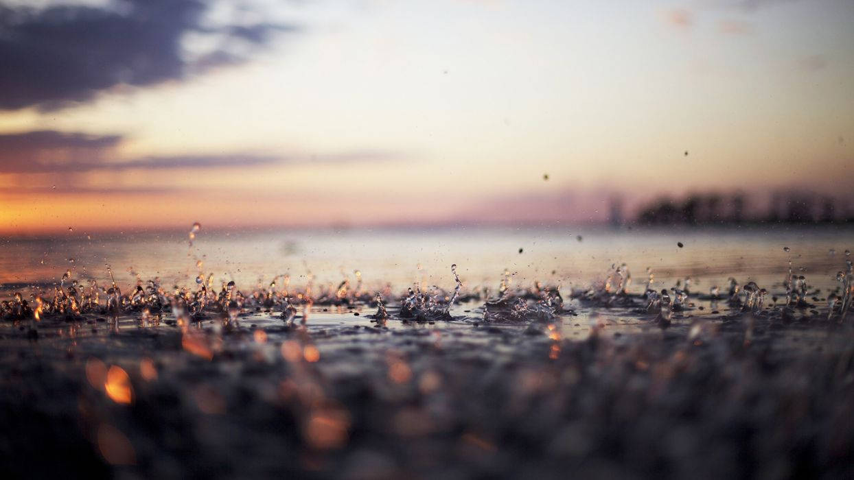 Rainy Day 桌布 壁紙 — 雨滴戲劇性地濺在濕地上，金色夕陽的光芒透過柔和的紫色雲朵在上方閃耀。
