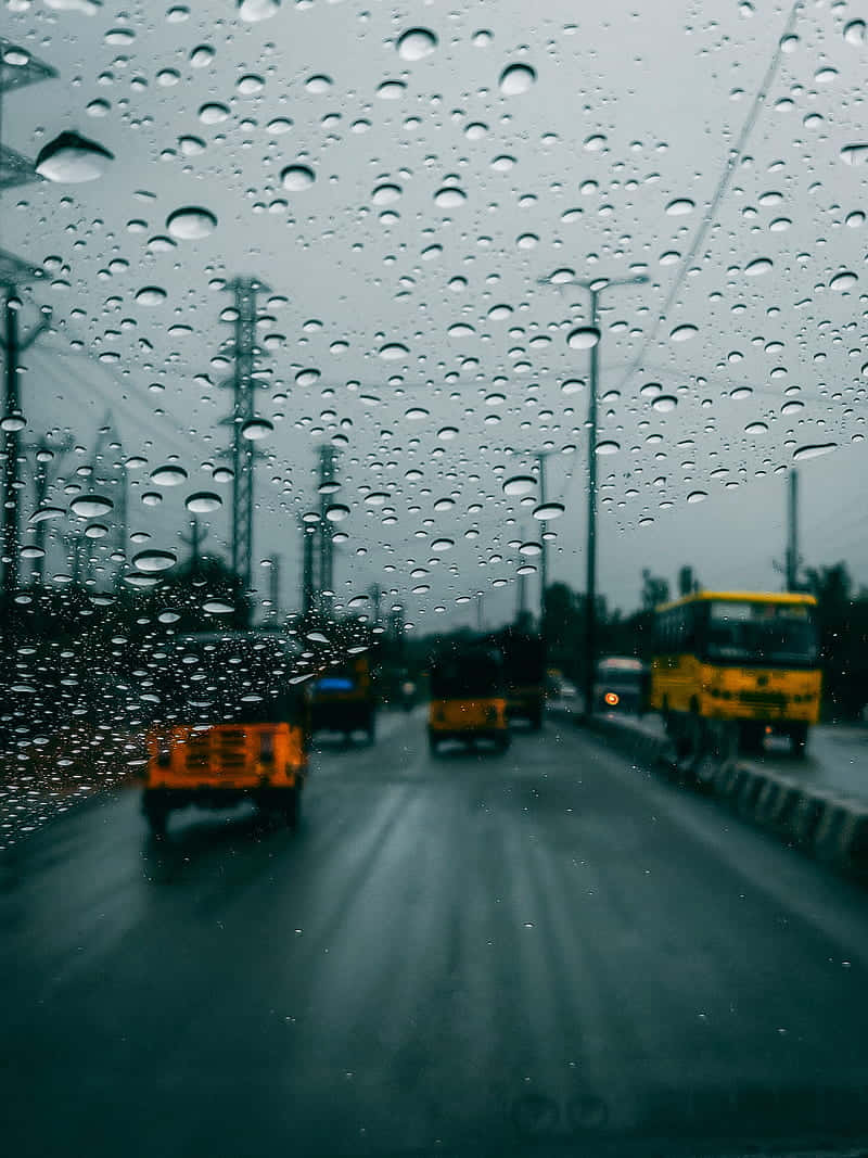 Rain Desktop 桌布 壁紙 — 雨滴模糊了濕漉漉的城市街道景象，黃色公車和卡車在灰濛濛的天空下行駛。