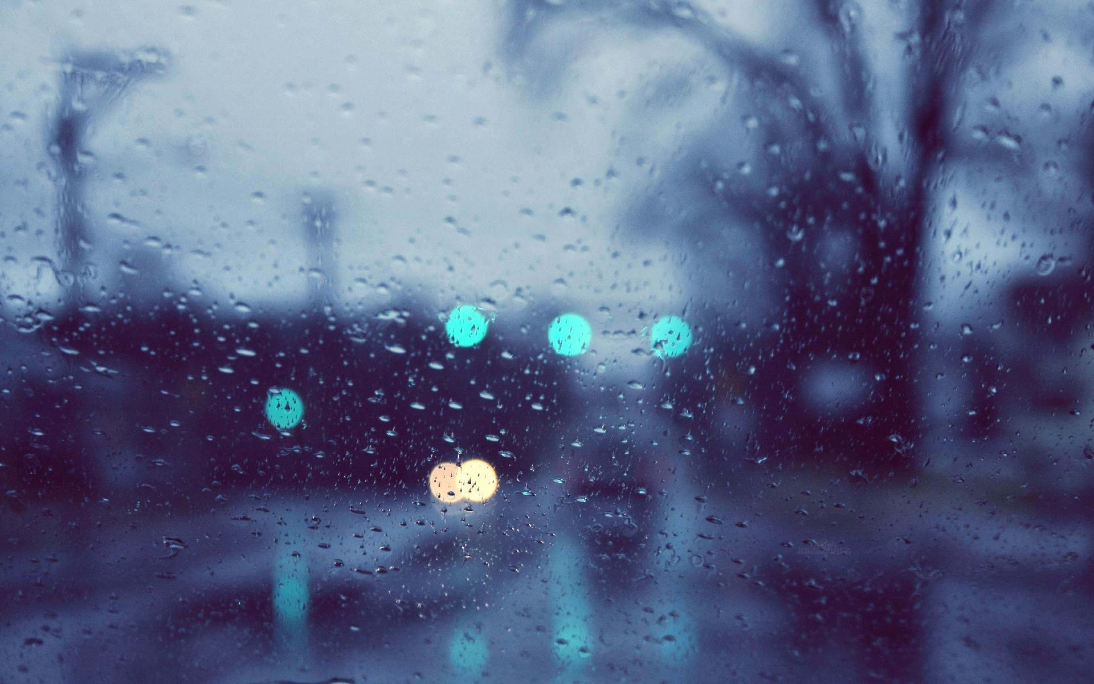 Raining 桌布 壁紙 — 雨滴模糊了窗外的景色，發光的青綠色和琥珀色燈光在雨中的城市場景中掠過。