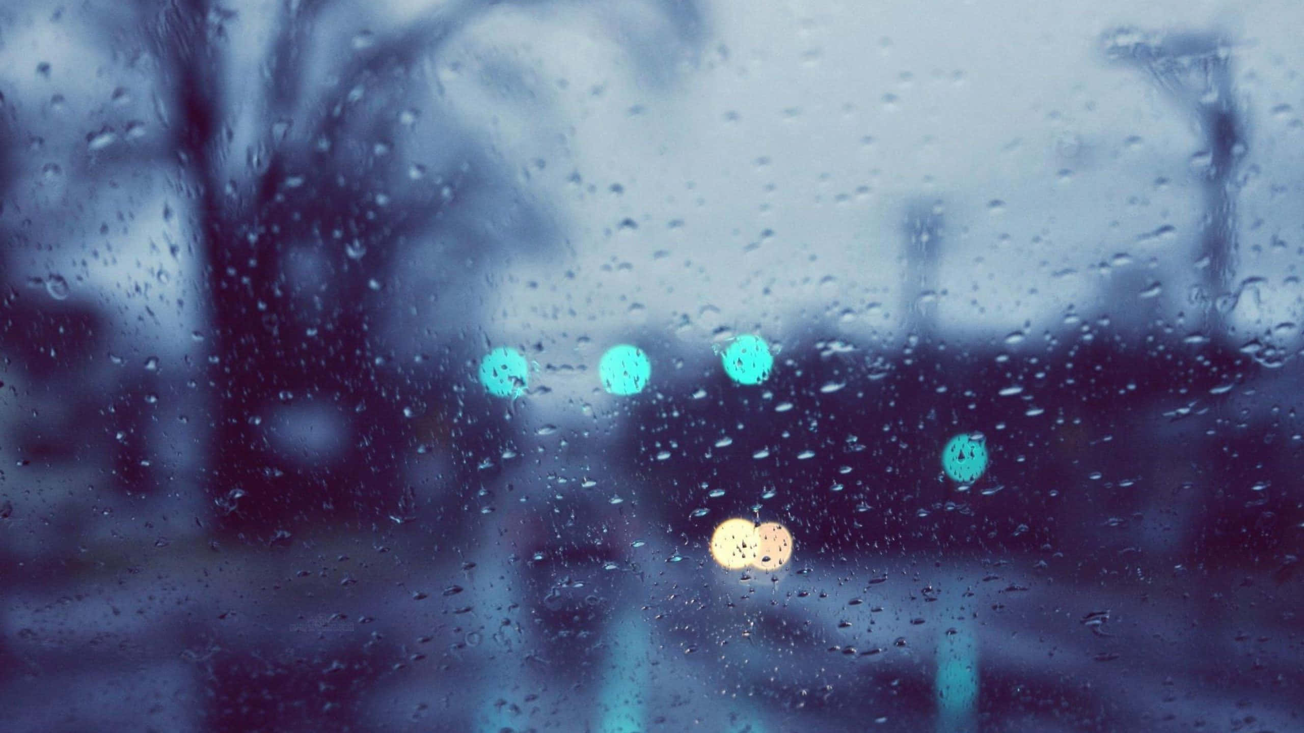 下雨 桌布 壁紙 — 雨滴模糊了窗外的景色，背景中閃爍的青綠色和琥珀色燈光柔和地劃過。
