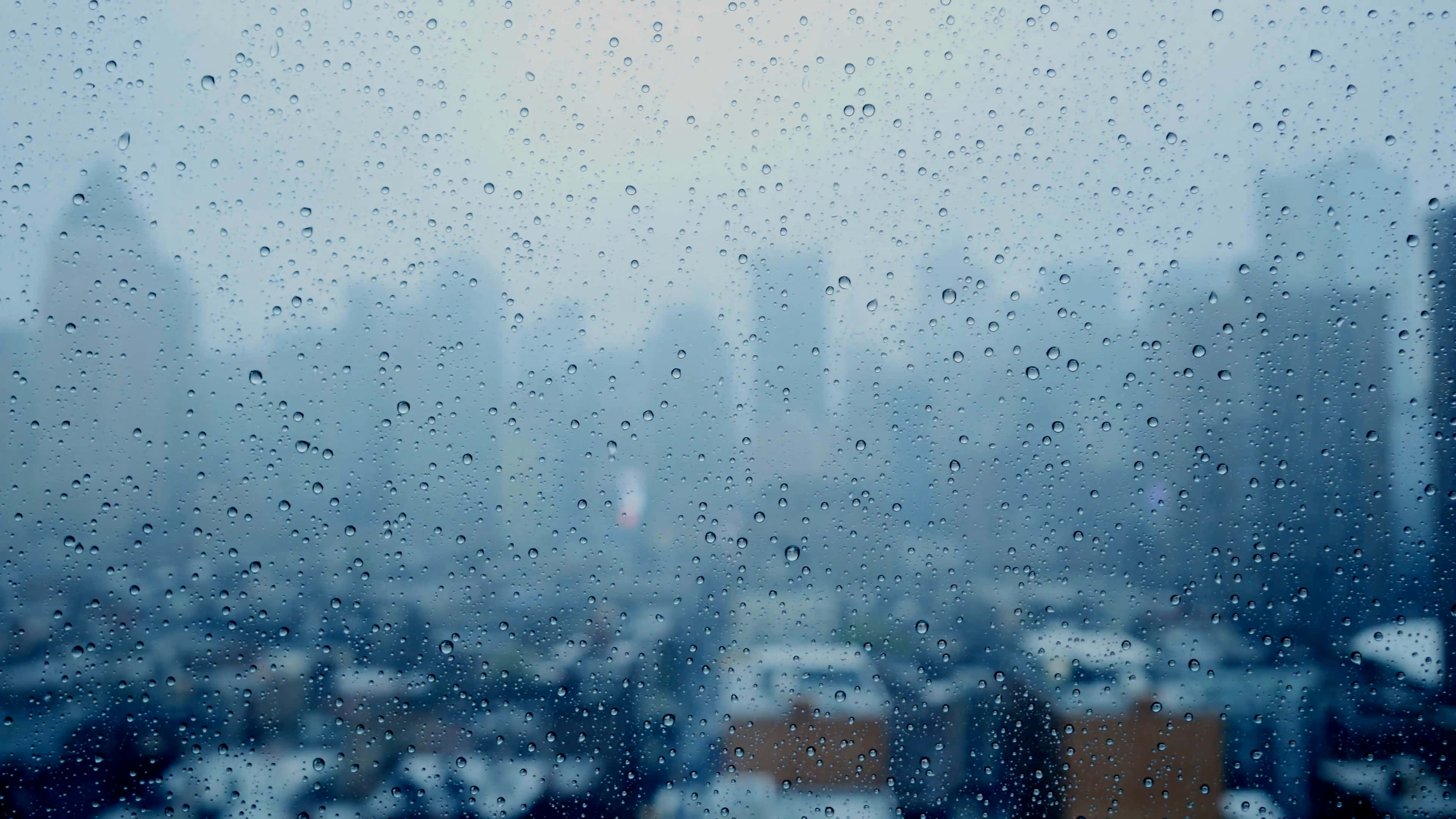 城市 桌布 壁紙 — 雨滴模糊了窗外的朦朧城市景觀，營造出憂鬱的冬日場景。