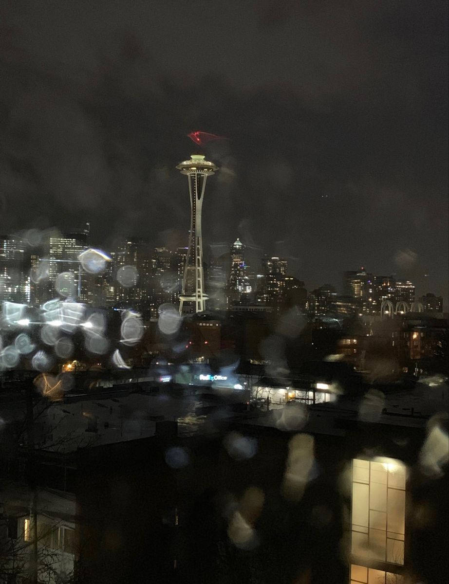Seattle Skyline 桌布 壁紙 — 雨滴模糊了西雅圖夜晚的天際線景觀，太空針塔在黑暗的天空下閃耀。