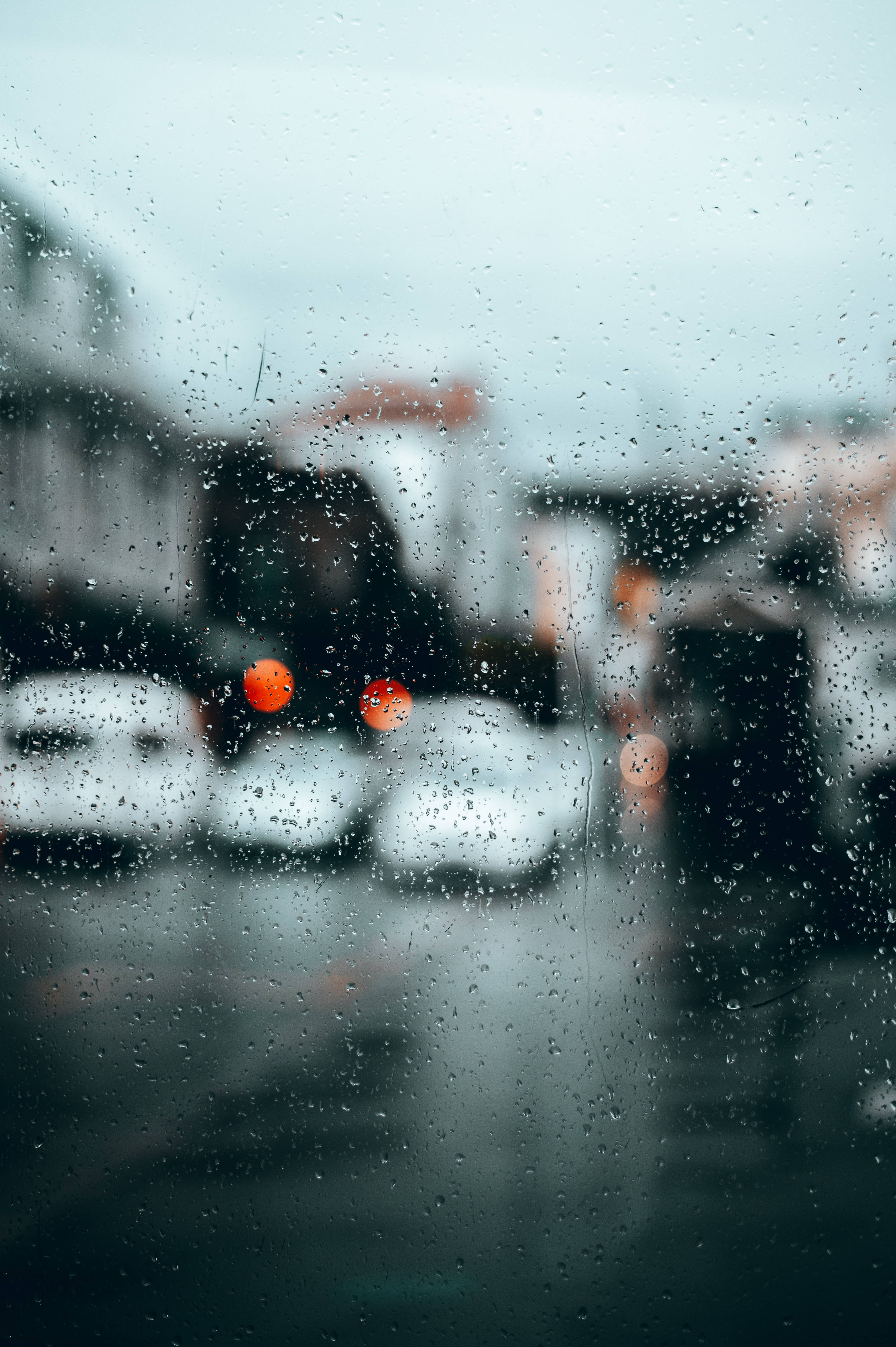 Transparent 桌布 壁紙 — 雨滴模糊了透過窗戶看到的城市街道景觀，遠處有發光的橙色汽車尾燈。