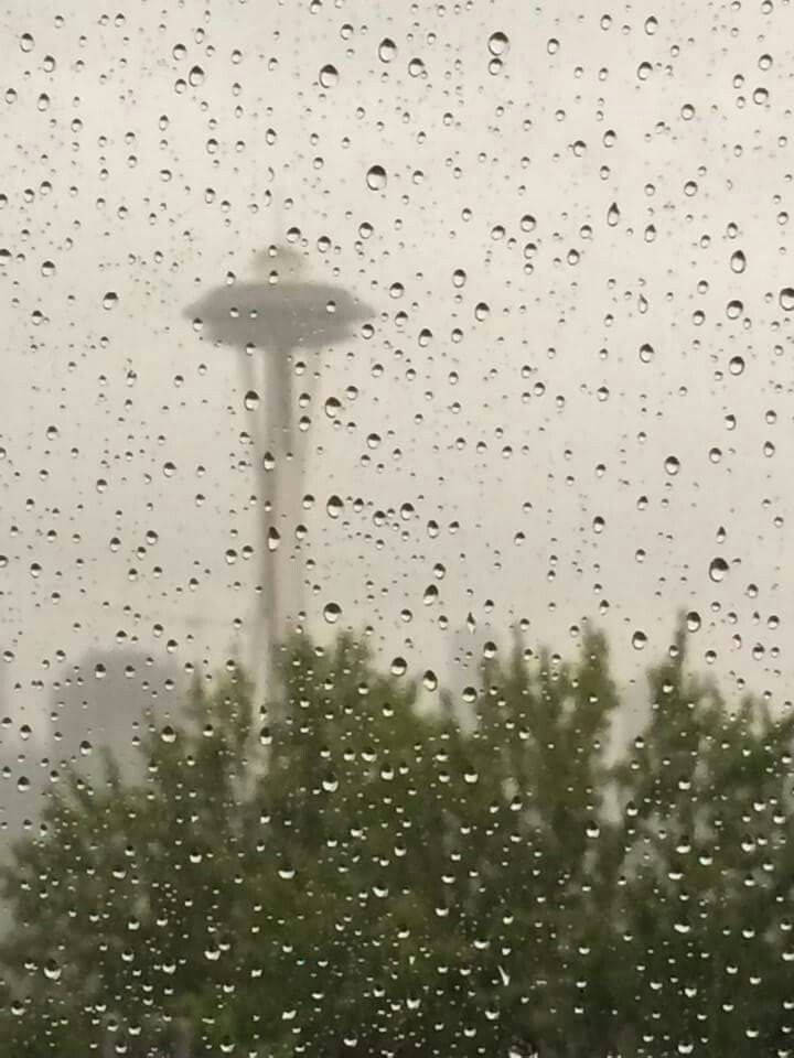 Rainy Day 桌布 壁紙 — 雨滴模糊了透過窗戶看到的太空針塔景觀，在灰濛濛的雨天裡，下方有綠樹。