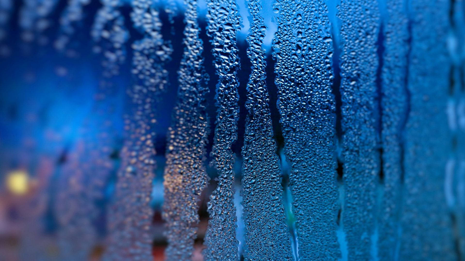 Water Drops 桌布 壁紙 — 雨滴沿玻璃滑落的特寫，背景有模糊的藍色和暖色燈光。
