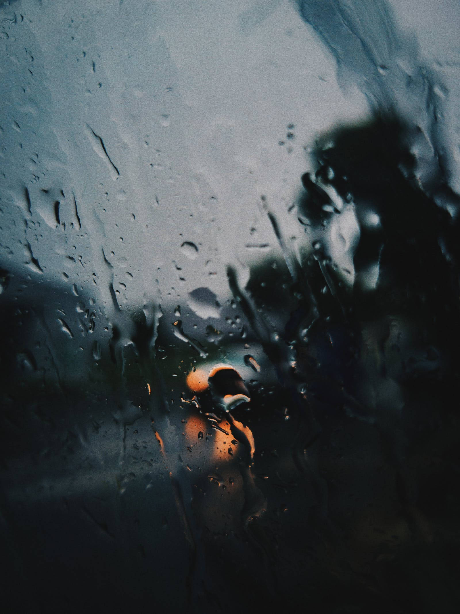 Raining 桌布 壁紙 — 雨滴沿窗戶流下，一個模糊的身影帶著溫暖的橙色光芒站在外面的陰暗處。