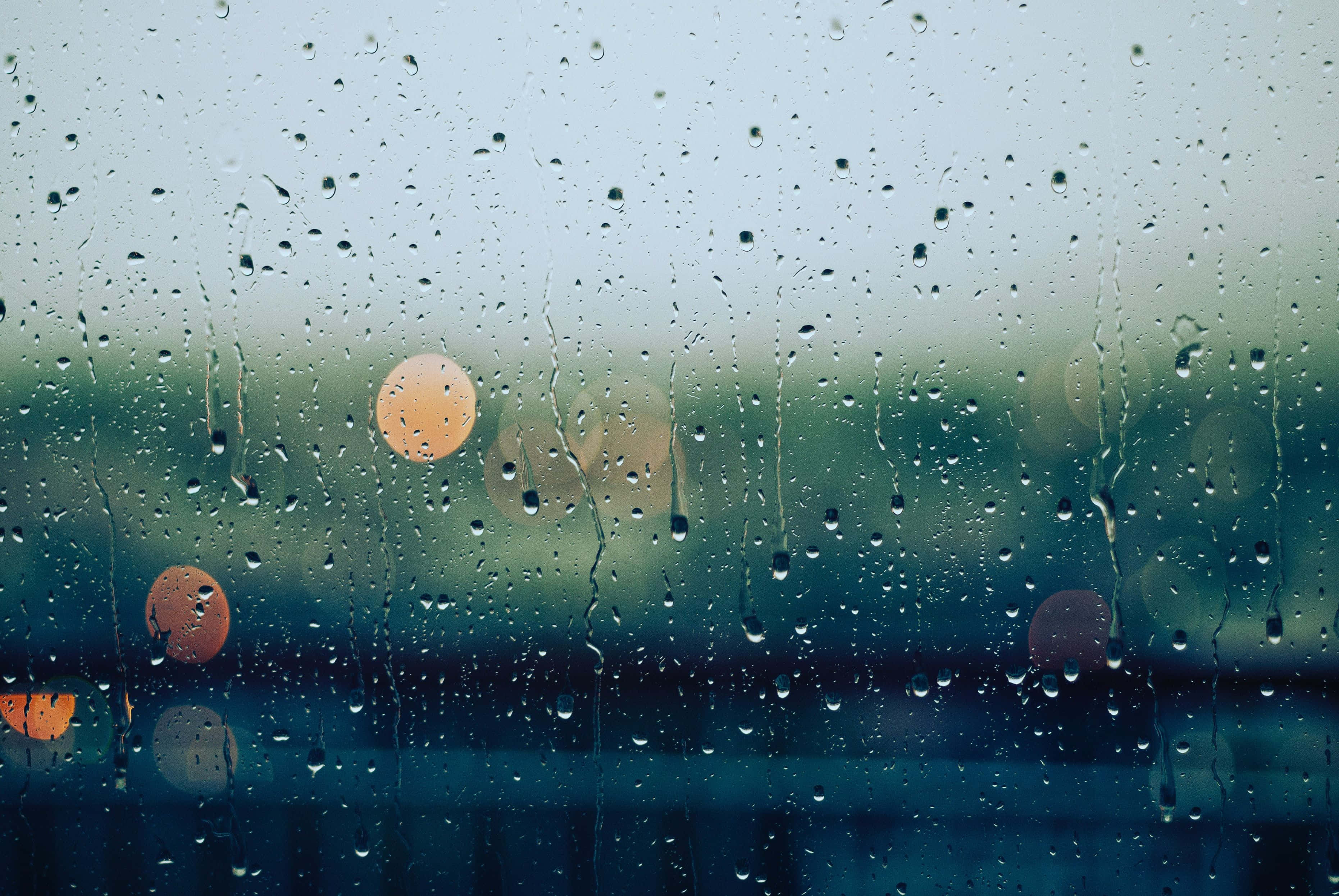 Rainy Day 桌布 壁紙 — 雨滴沿窗戶流下，在清涼的藍綠色背景上顯現出模糊的溫暖燈光。