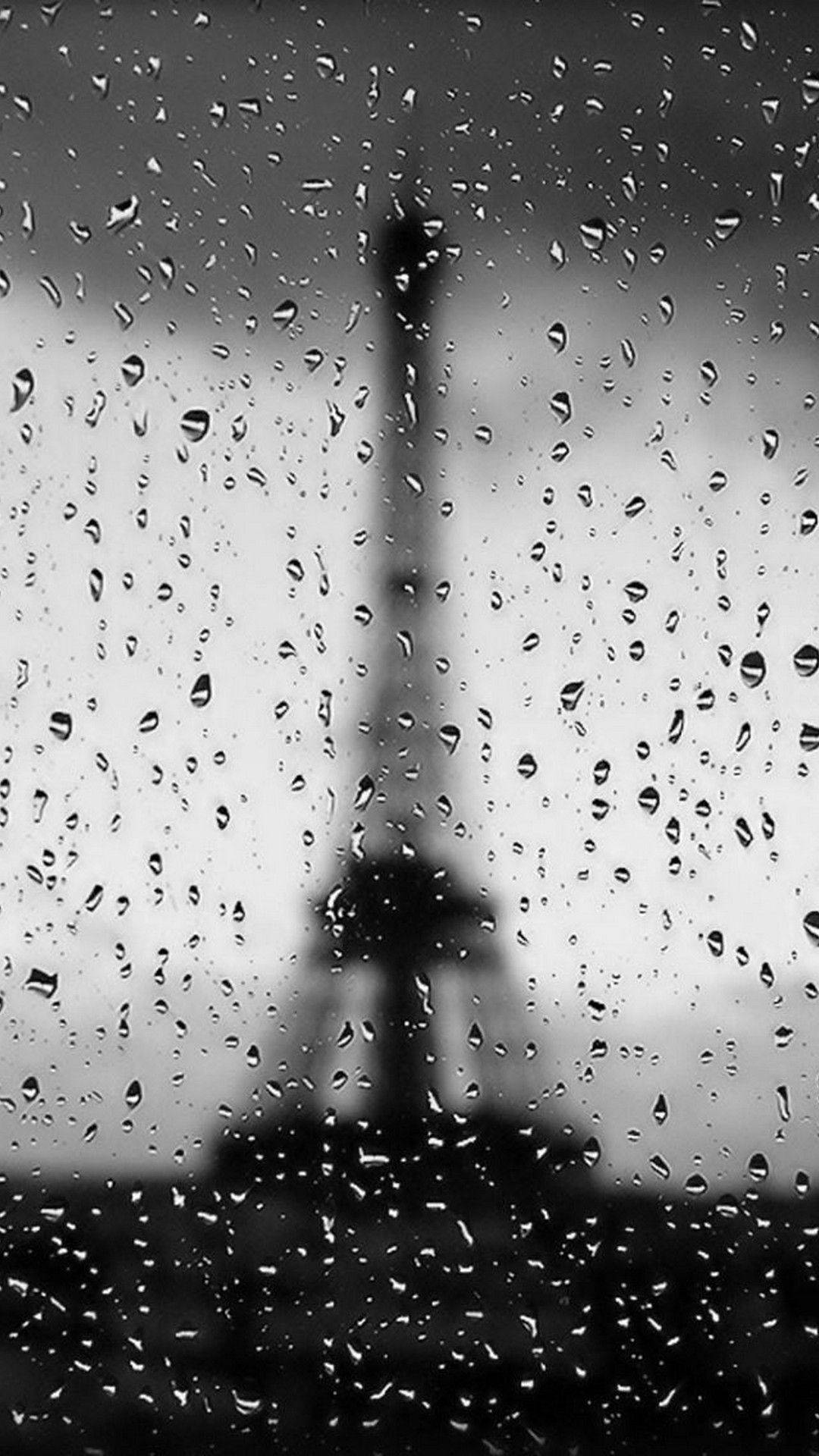 Eiffel Tower 桌布 壁紙 — 雨滴沿窗戶流下，顯現出灰色天空背景下模糊的艾菲爾鐵塔輪廓。