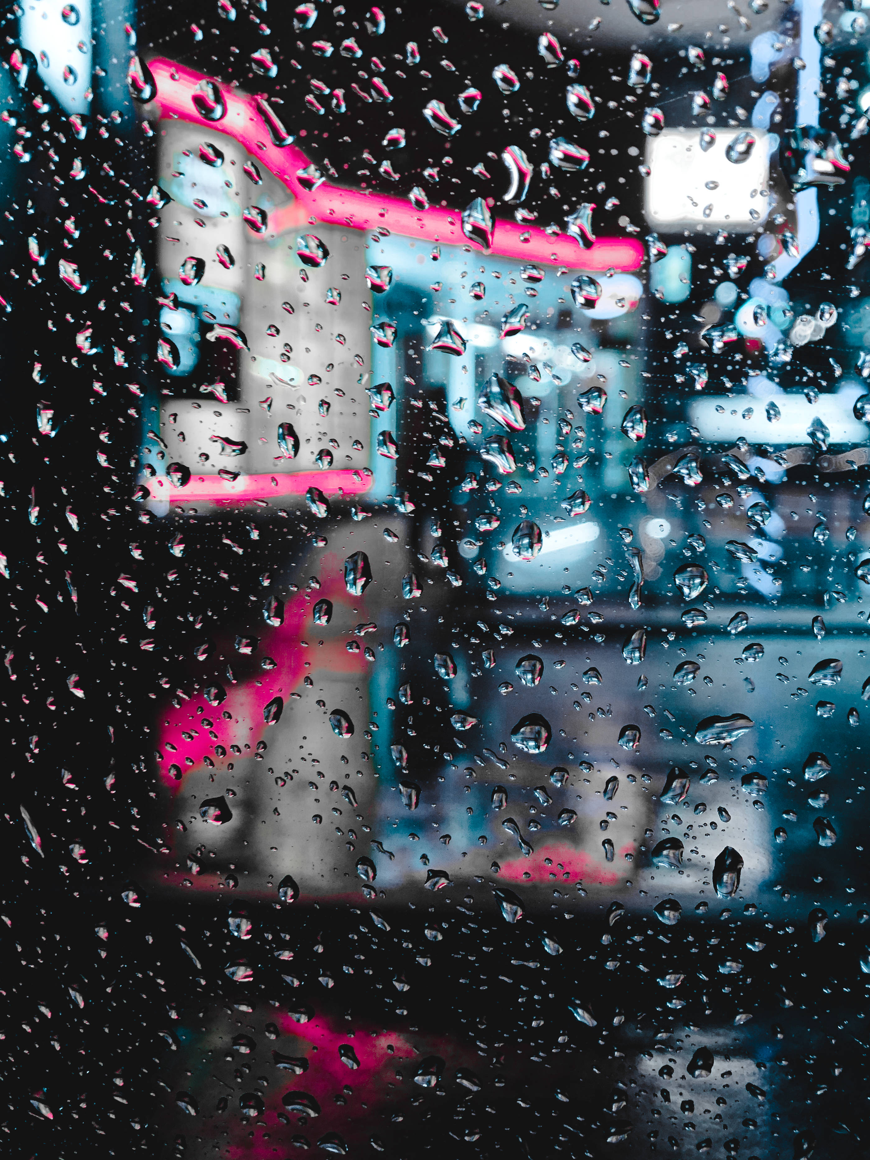 dark neon iPhone 桌布 壁紙 — 雨滴沿窗戶流下，顯露出夜間城市模糊的霓虹燈光。