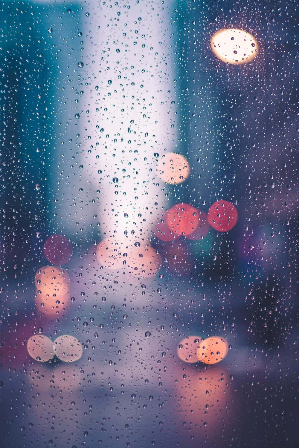 window 桌布 壁紙 — 雨滴沿窗戶流下，顯露出模糊的城市燈光，在清涼的藍色暮色背景下溫暖地發光。