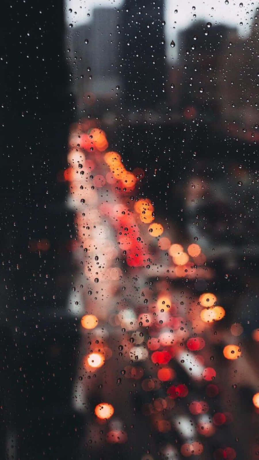 Aesthetic Rain 桌布 壁紙 — 雨滴沿窗戶流下，顯露出模糊的城市燈光，在黑暗的城市背景下溫暖地閃耀。