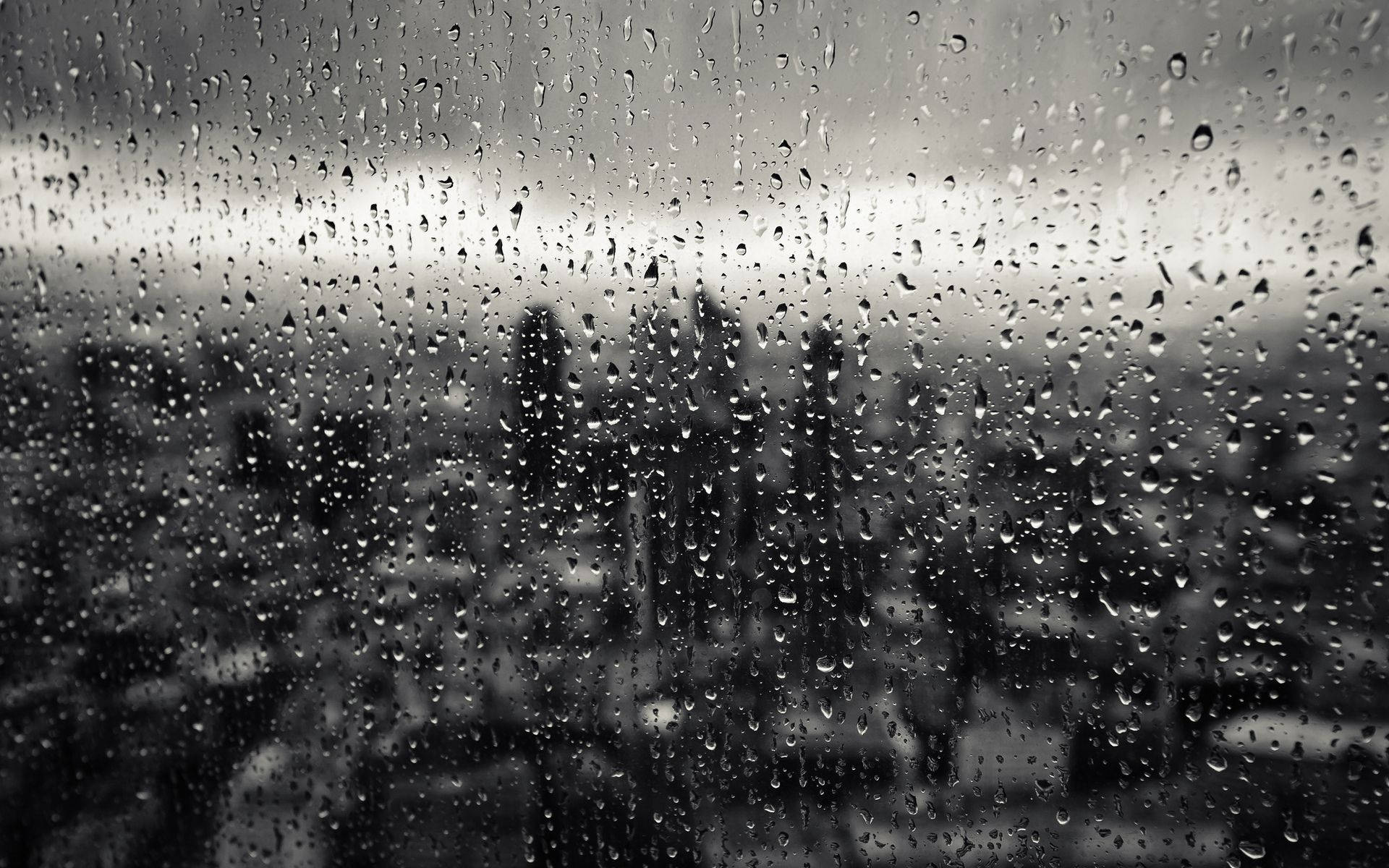 窗戶上的雨滴，俯瞰著灰色調的模糊城市。 — 下雨 GIF 壁紙