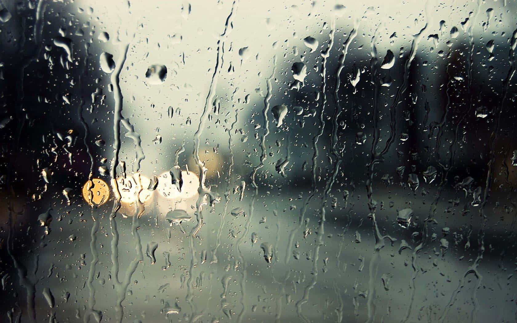 Rain Drops 桌布 壁紙 — 雨滴沿著汽車窗戶流下，將溫暖的路燈模糊成柔和發光的光球，映襯著灰色的城市背景。