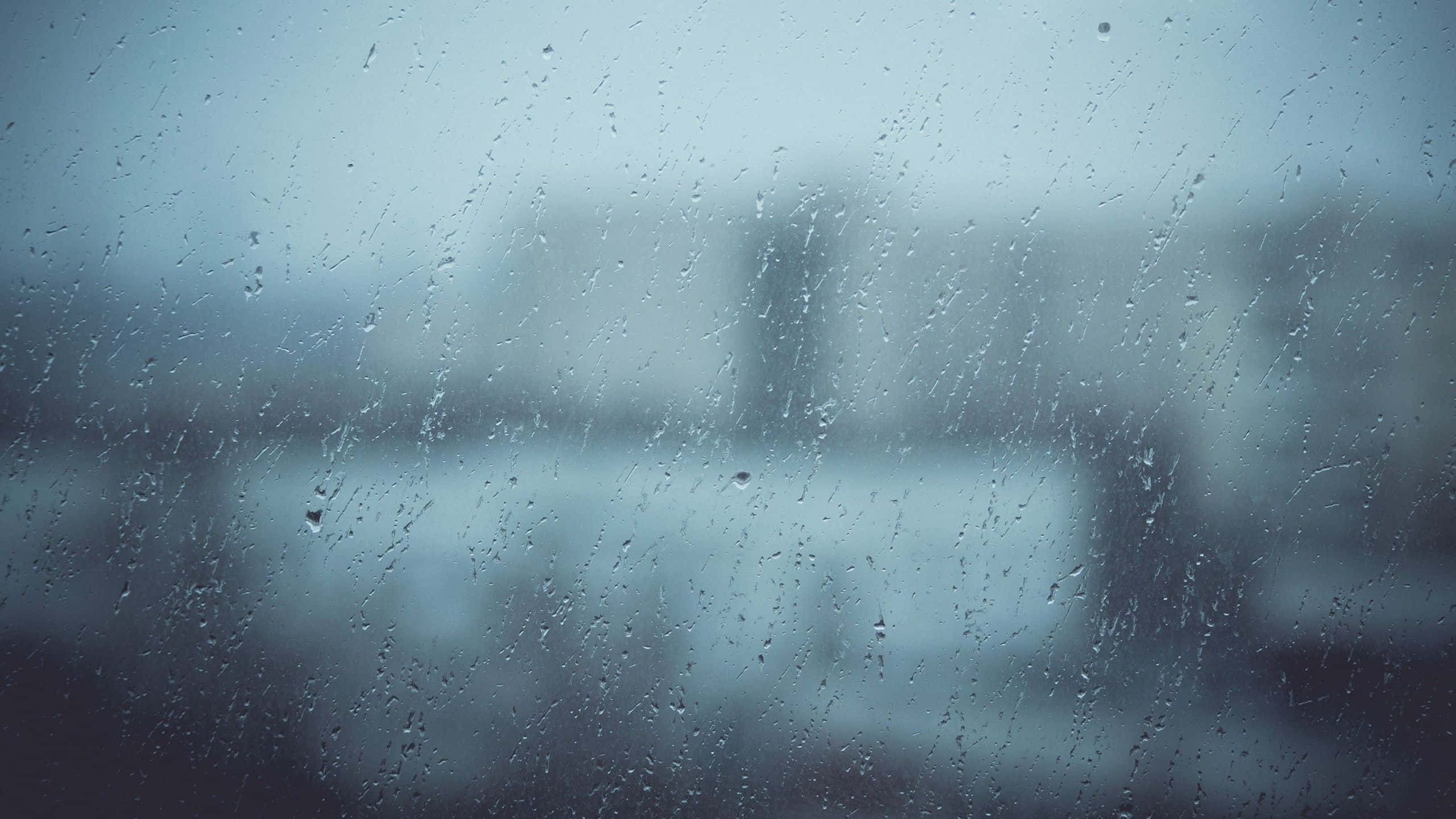 Rainy 桌布 壁紙 — 雨滴沿著玻璃窗流下，模糊了冷藍色調中沉悶的城市景觀。