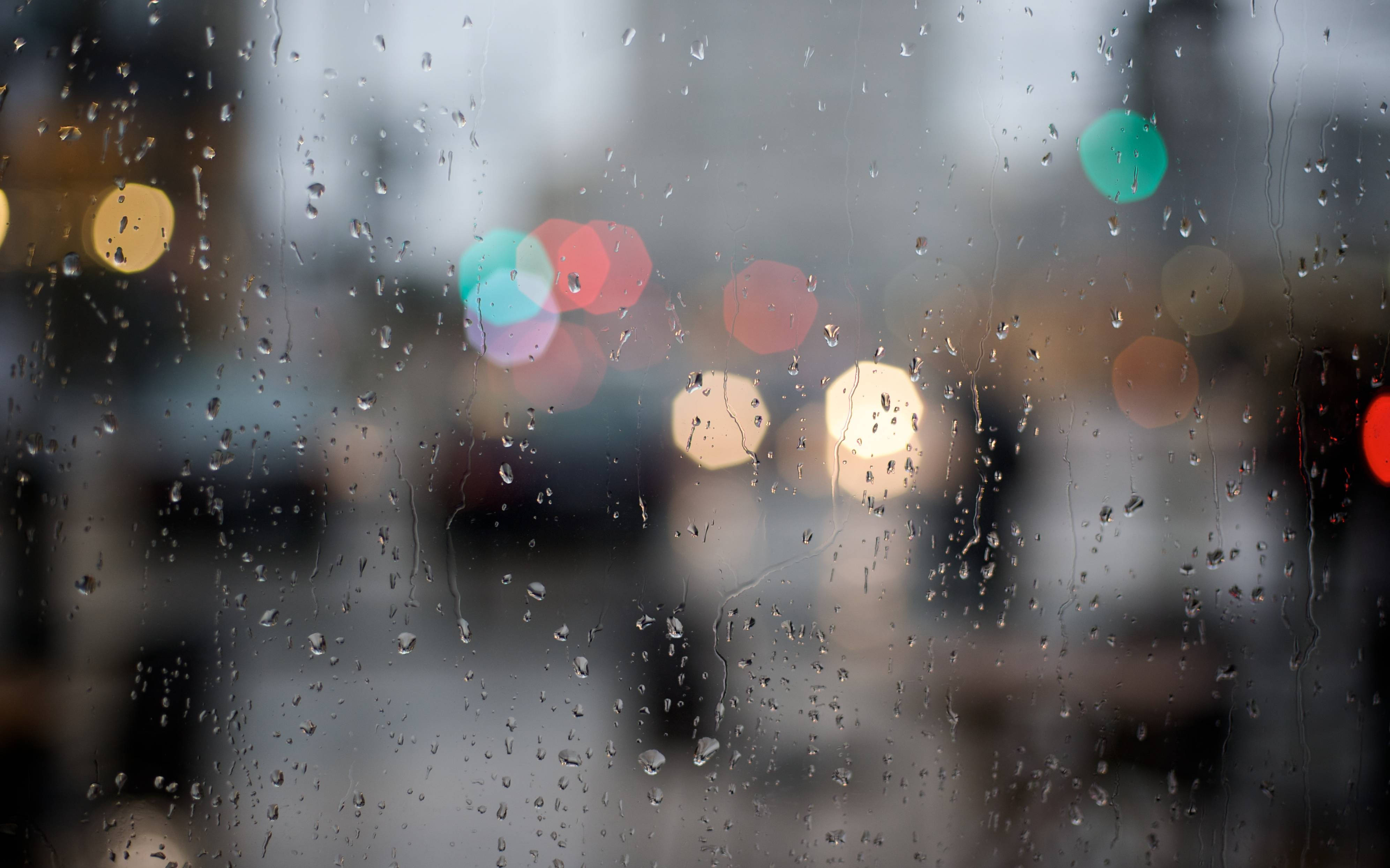 Rainy Day 桌布 壁紙 — 雨滴沿著玻璃窗流下，背景中模糊的城市燈光溫暖地閃爍。