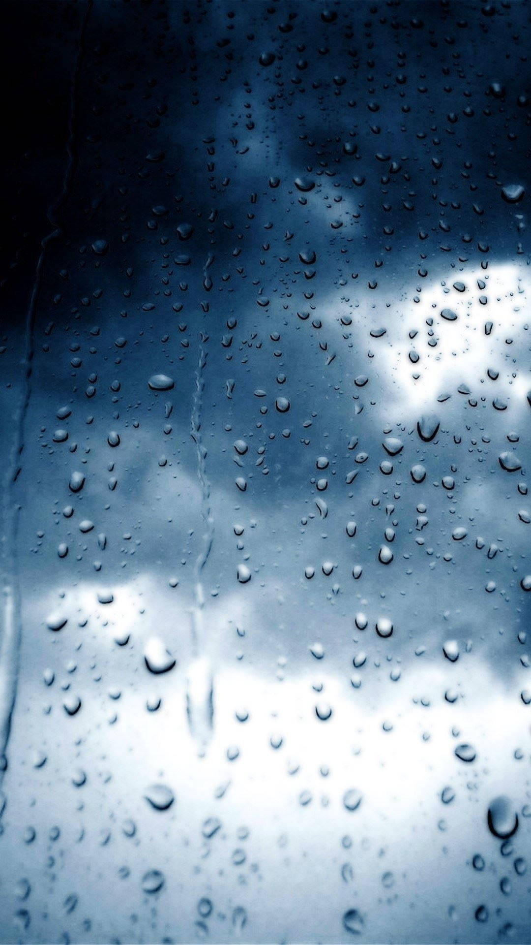 暴風 桌布 壁紙 — 雨滴沿著玻璃窗流下，露出陰沉多雲的天空，帶有冷藍色調。