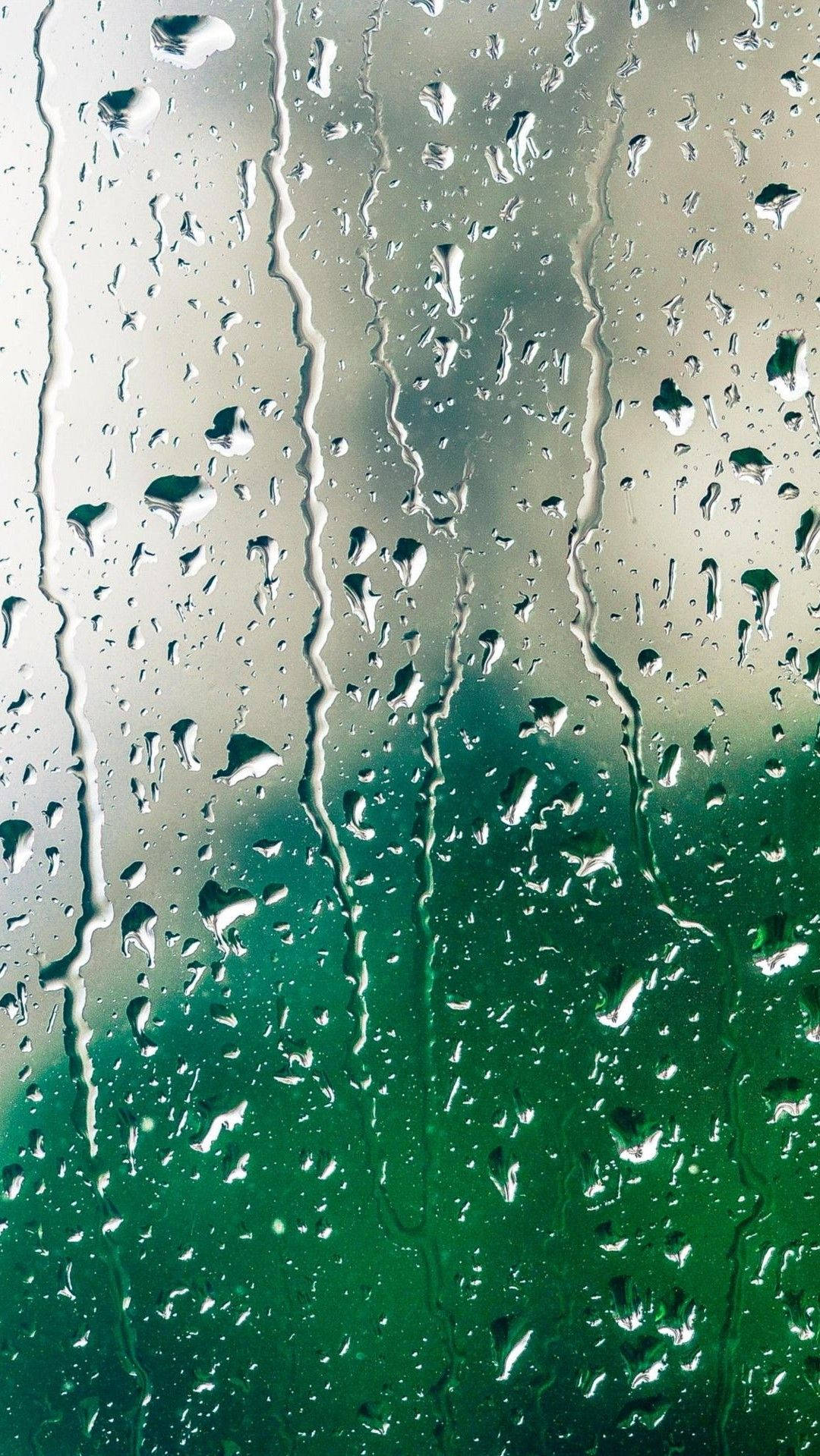WhatsApp 聊天 桌布 壁紙 — 雨滴沿著玻璃窗流下，顯露出模糊的綠色和灰色戶外景色。