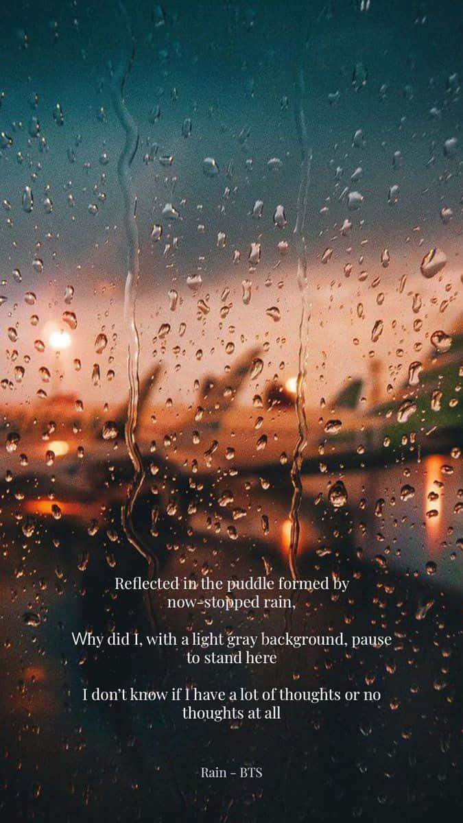 桌布 壁紙 — 雨滴沿著窗戶流下，框住黃昏時模糊的城市景觀，溫暖的路燈透過濕玻璃閃爍。
