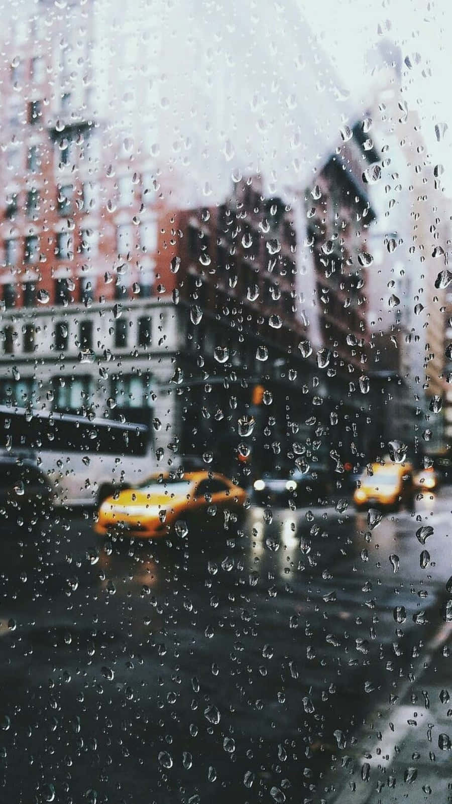 Aesthetic Rain 桌布 壁紙 — 雨滴沿著窗戶流下，窗外是模糊的城市街道，有黃色的士和磚砌建築。